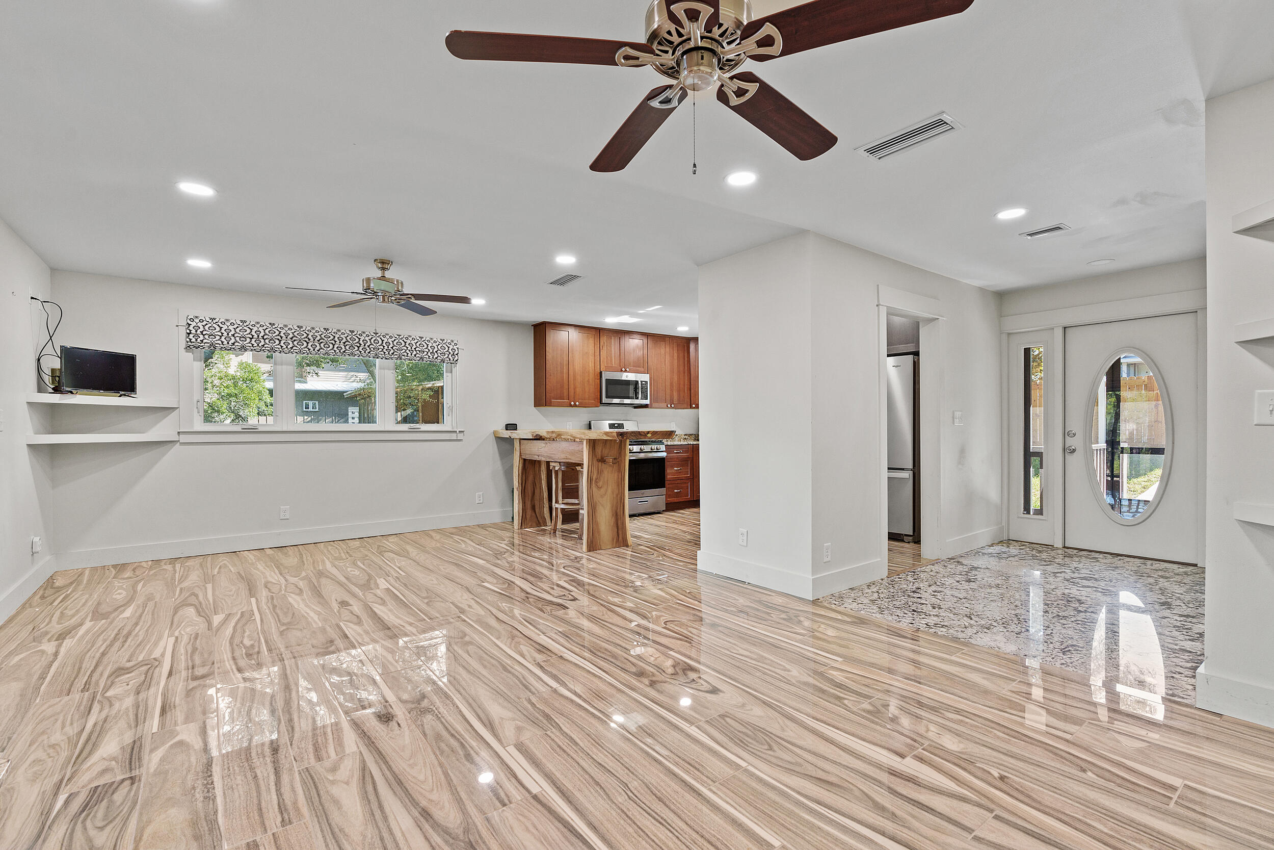 Open living area and kitchen with glossy wood-look tile floors, wood cabinets, and an oval-window front door.