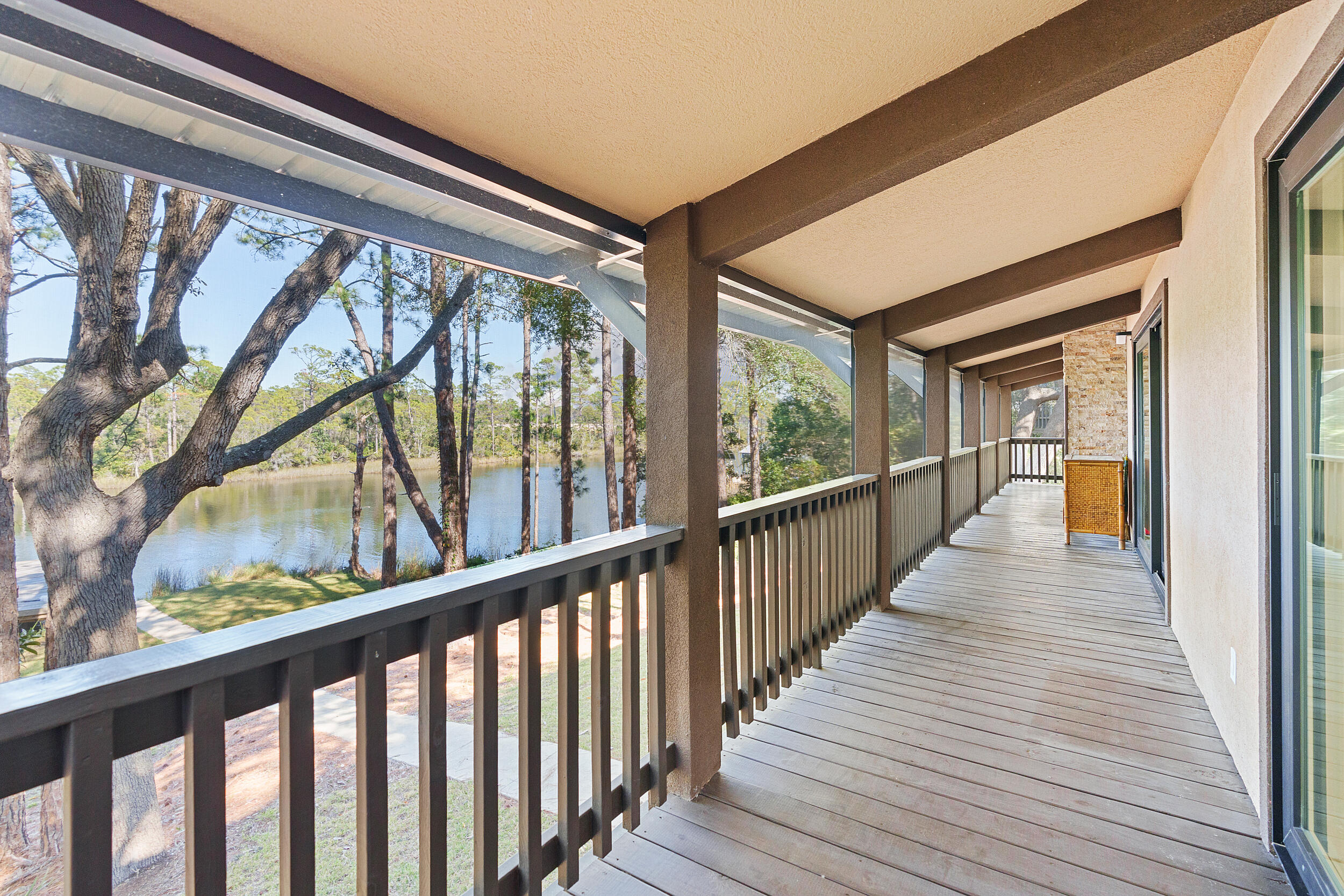 Covered lakeside porch with dark railings, wood decking, mature trees, and a calm water view.