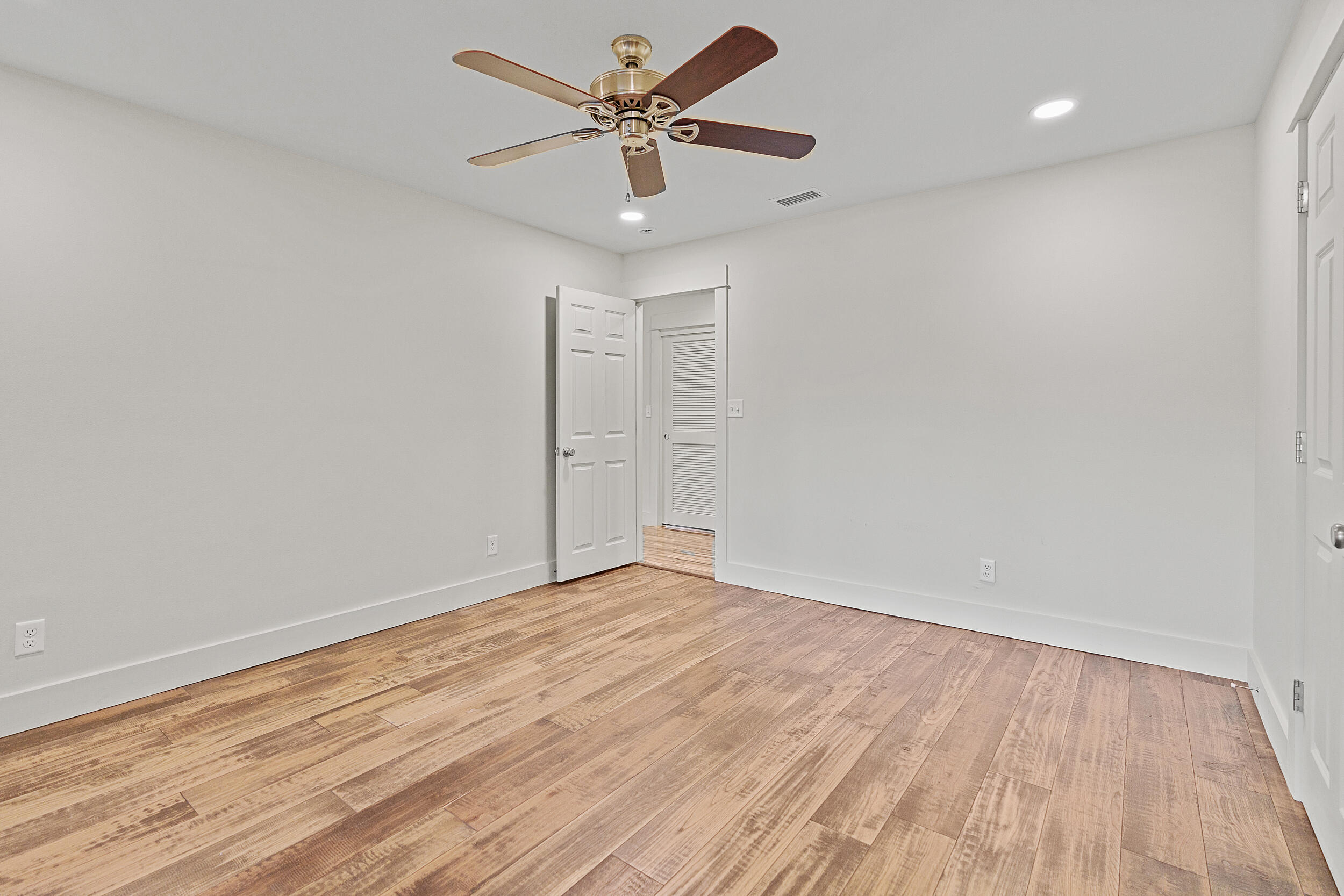 Empty room with wide-plank wood floors, a ceiling fan, and an open louvered closet door.