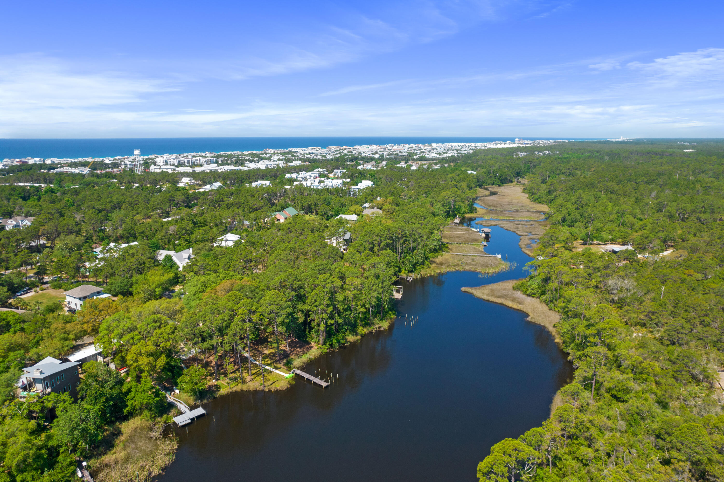 Aerial view of a wooded coastal waterway with homes, docks, and the Gulf in the distance.