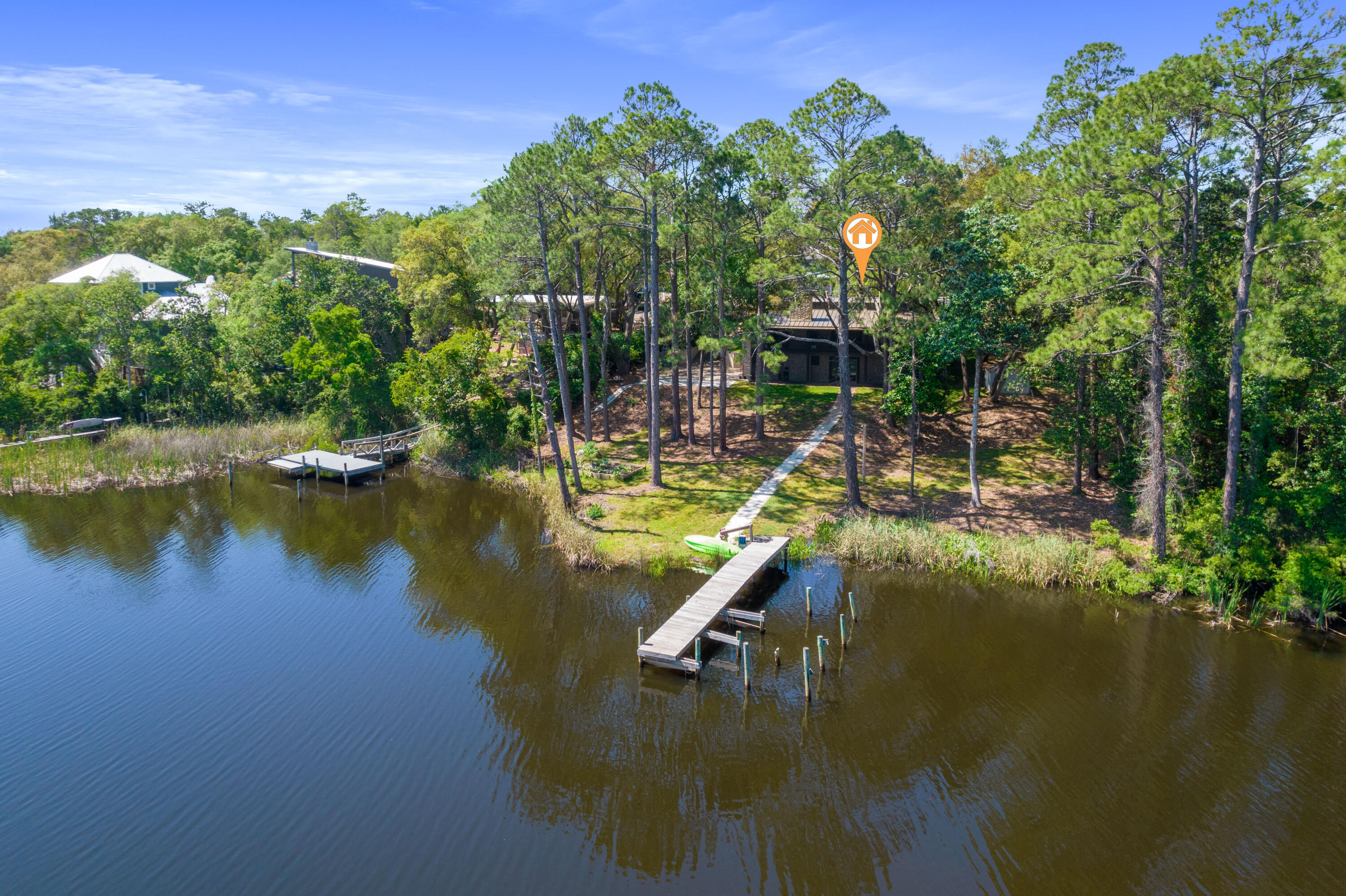 Aerial view of a wooded waterfront home with a long dock extending into the water.