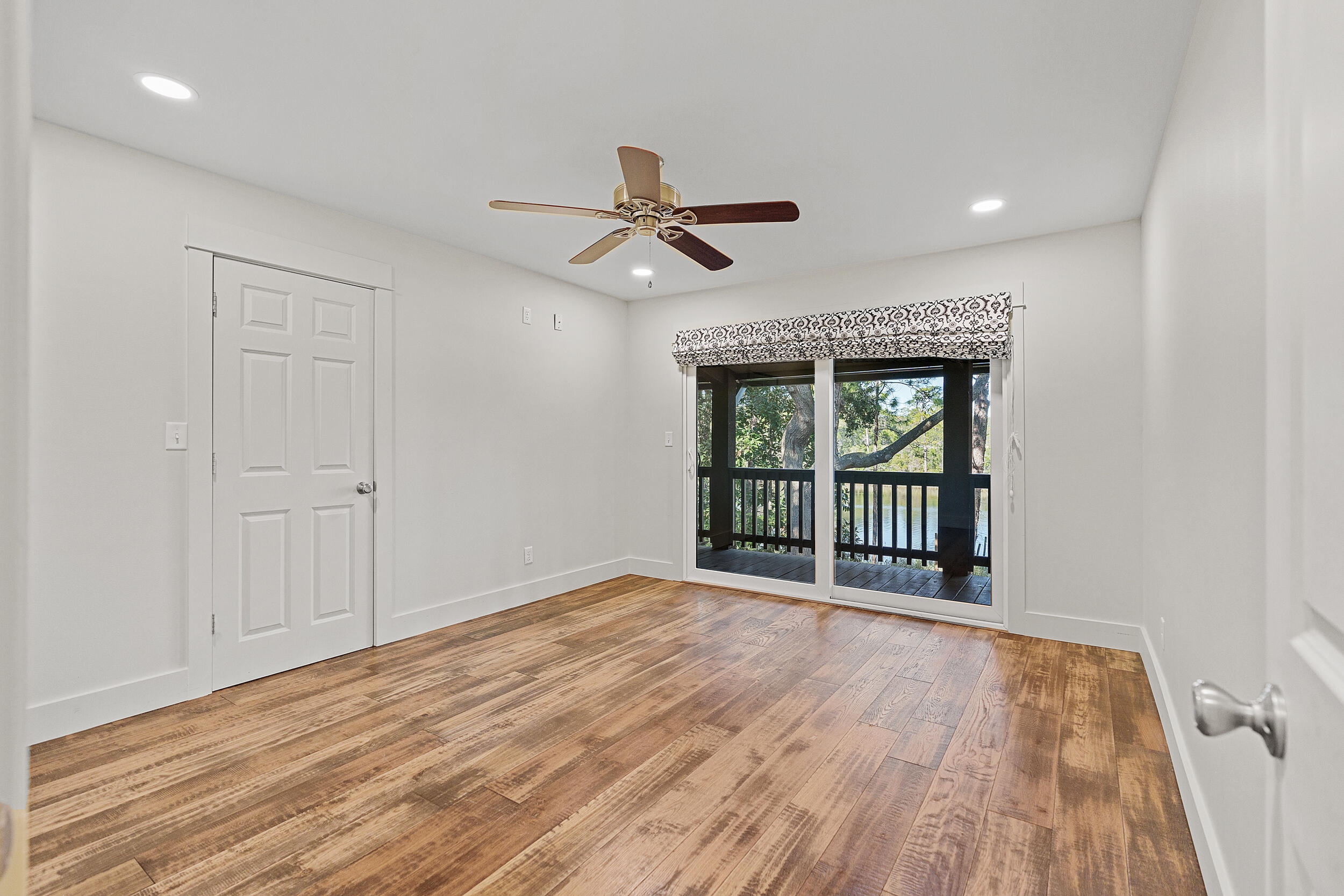 Vacant bedroom with rustic wood flooring and sliding doors overlooking a tree-lined porch and water.