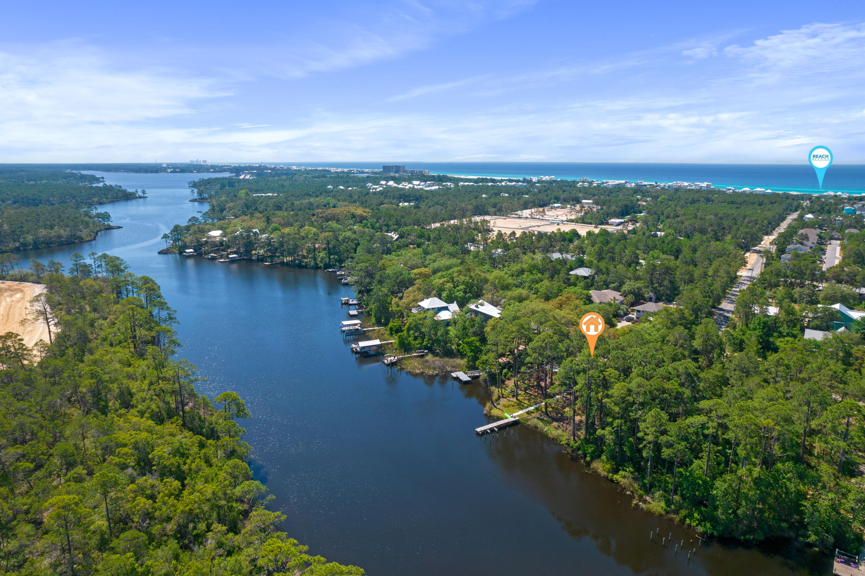 Aerial view of a wooded inlet property with shoreline docks and the Gulf beach in the distance.