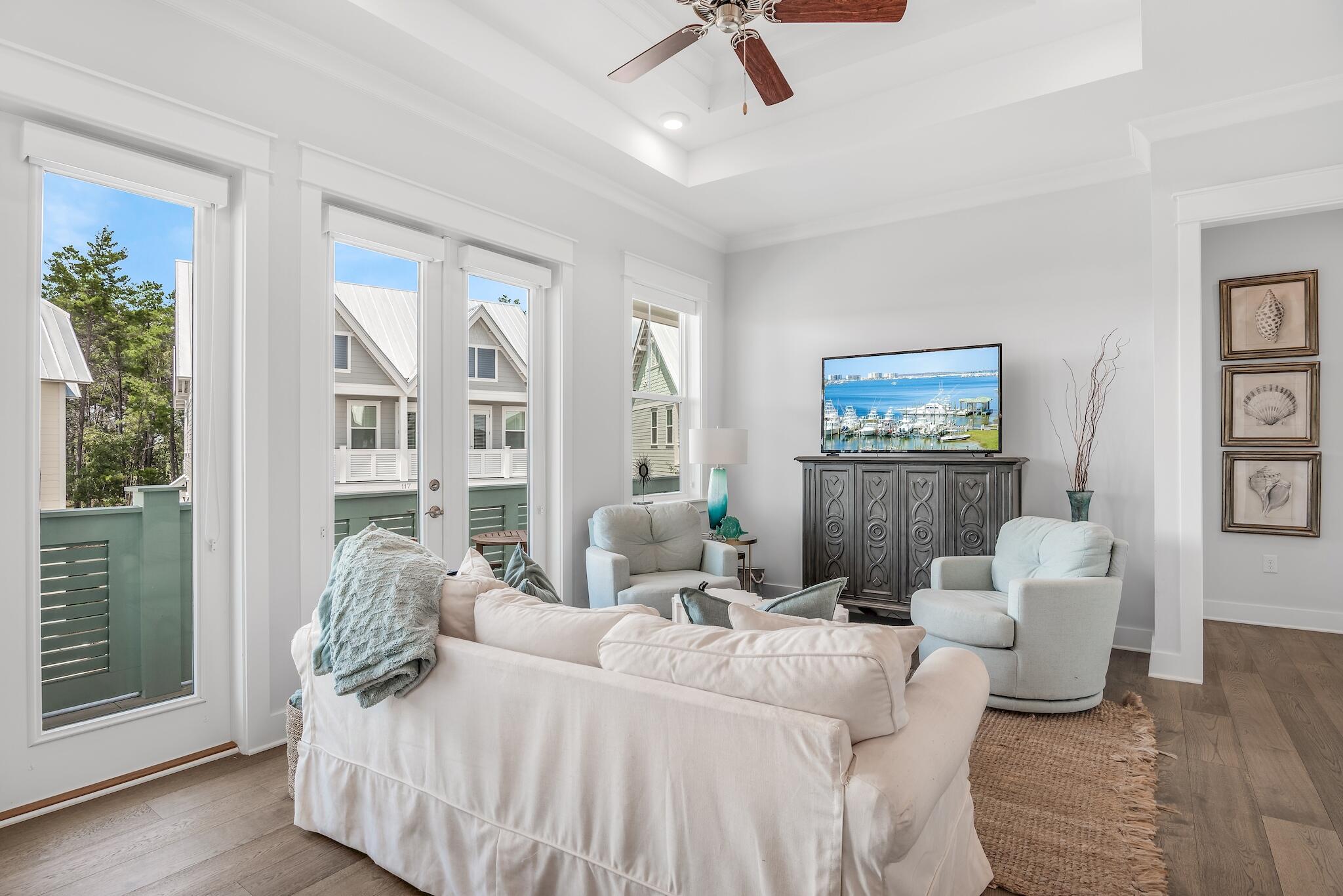 Bright furnished living room with balcony doors, pale seating, and a tray ceiling.