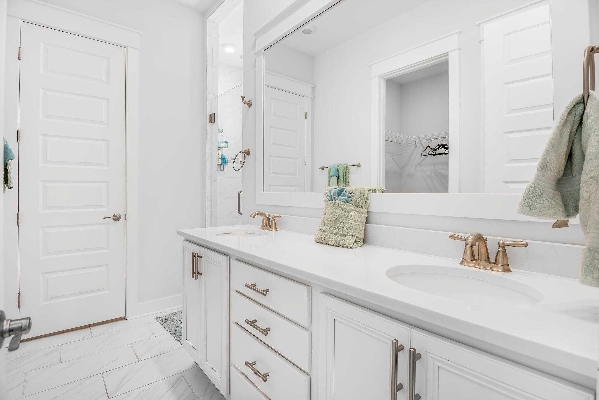 Bright white bathroom with a double-sink vanity, brass faucets, and a large mirror.