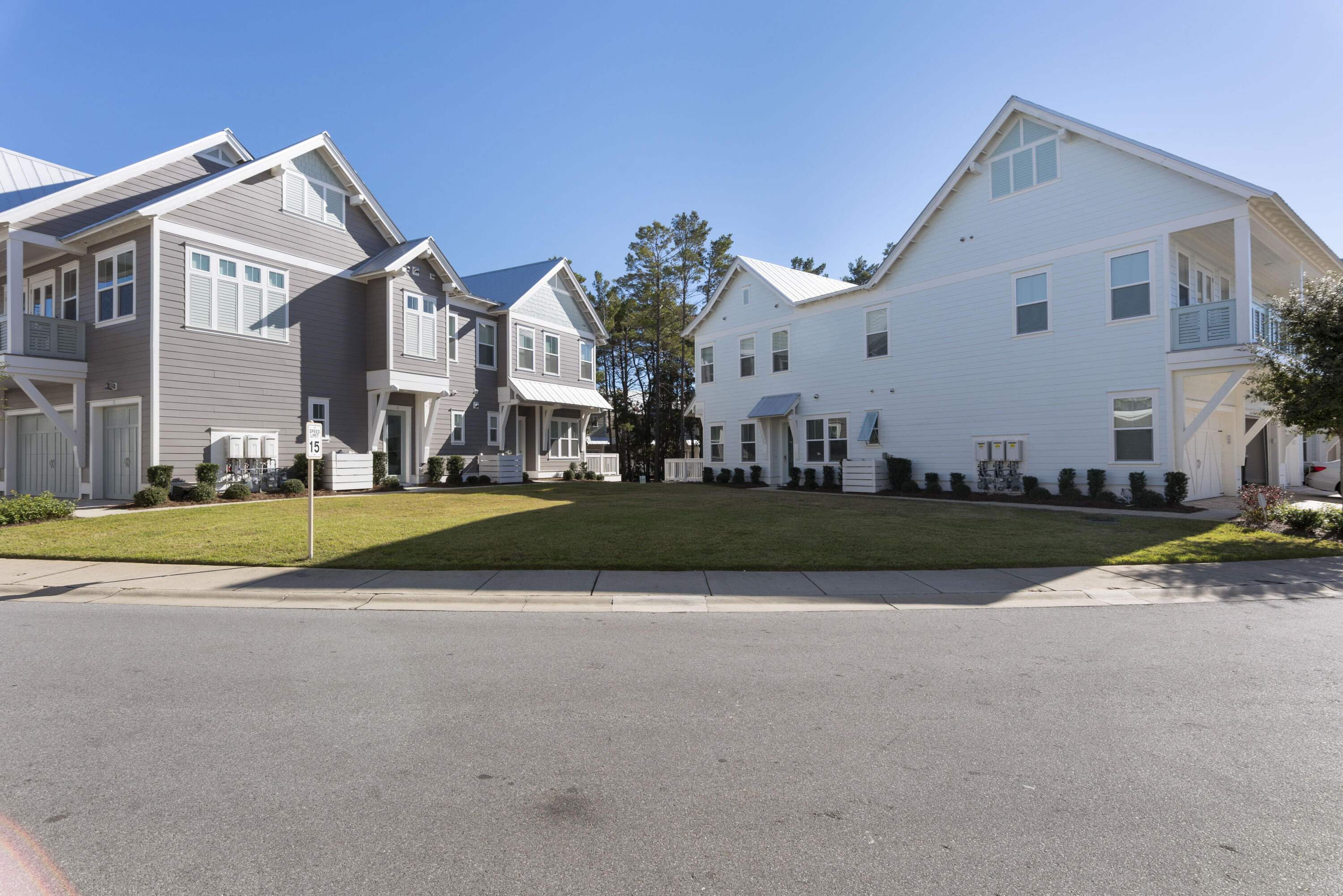 Attached gray and white townhomes with metal roofs and balconies facing a shared lawn.