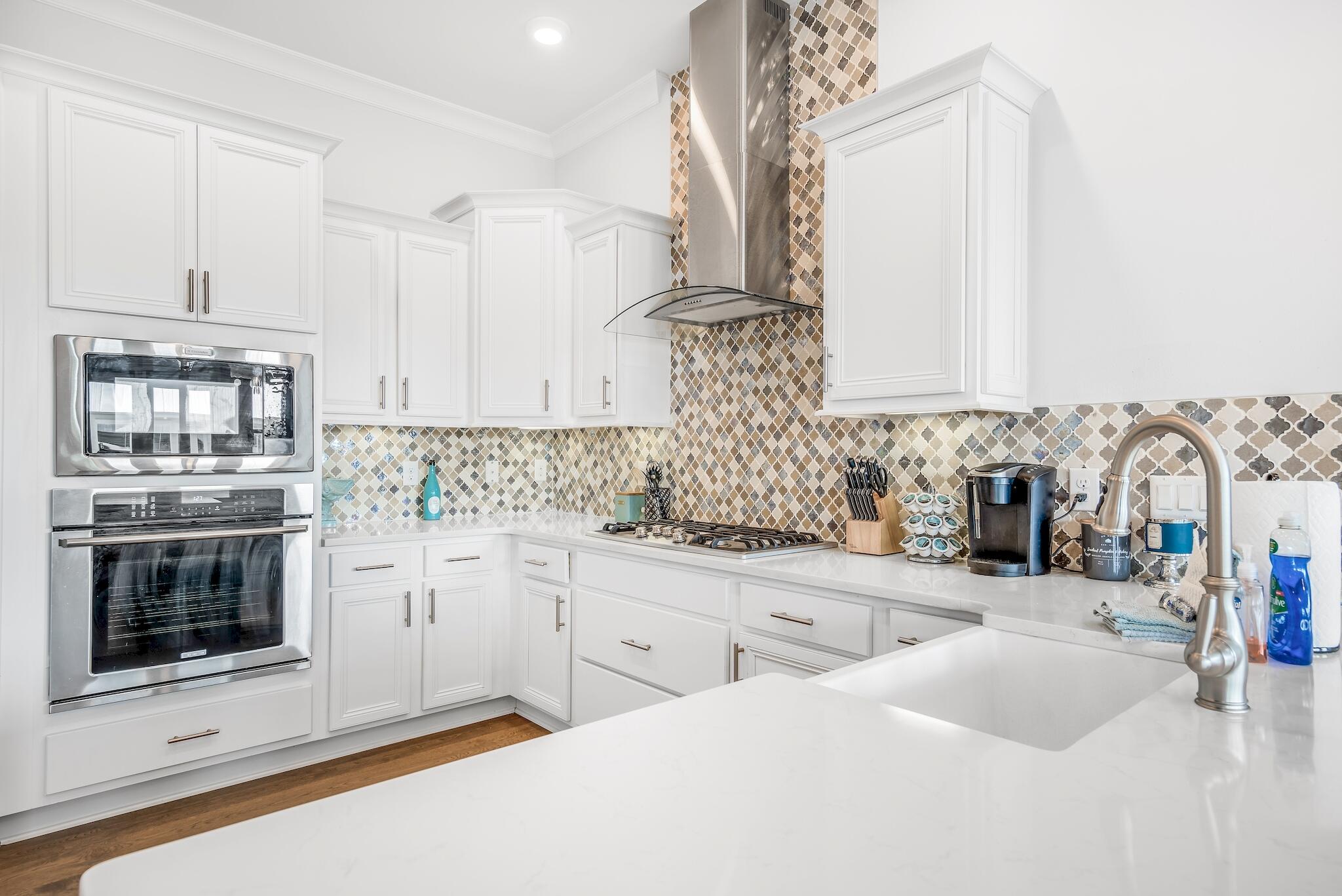 Kitchen with white cabinets, patterned tile backsplash, stainless steel appliances, and a large island sink.