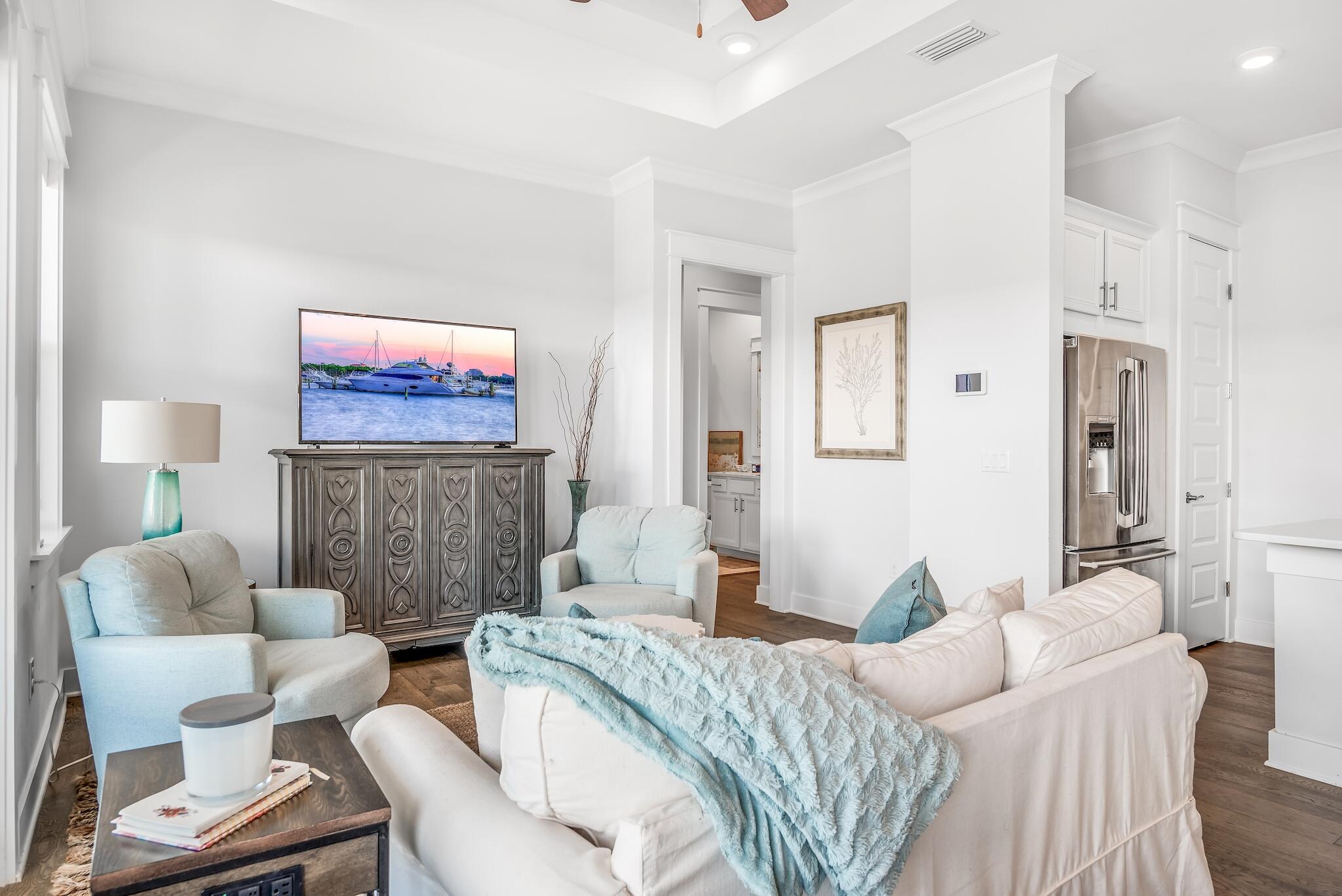 Open-plan living room with white sofas, pale blue chairs, and a carved wood media cabinet beside the kitchen.