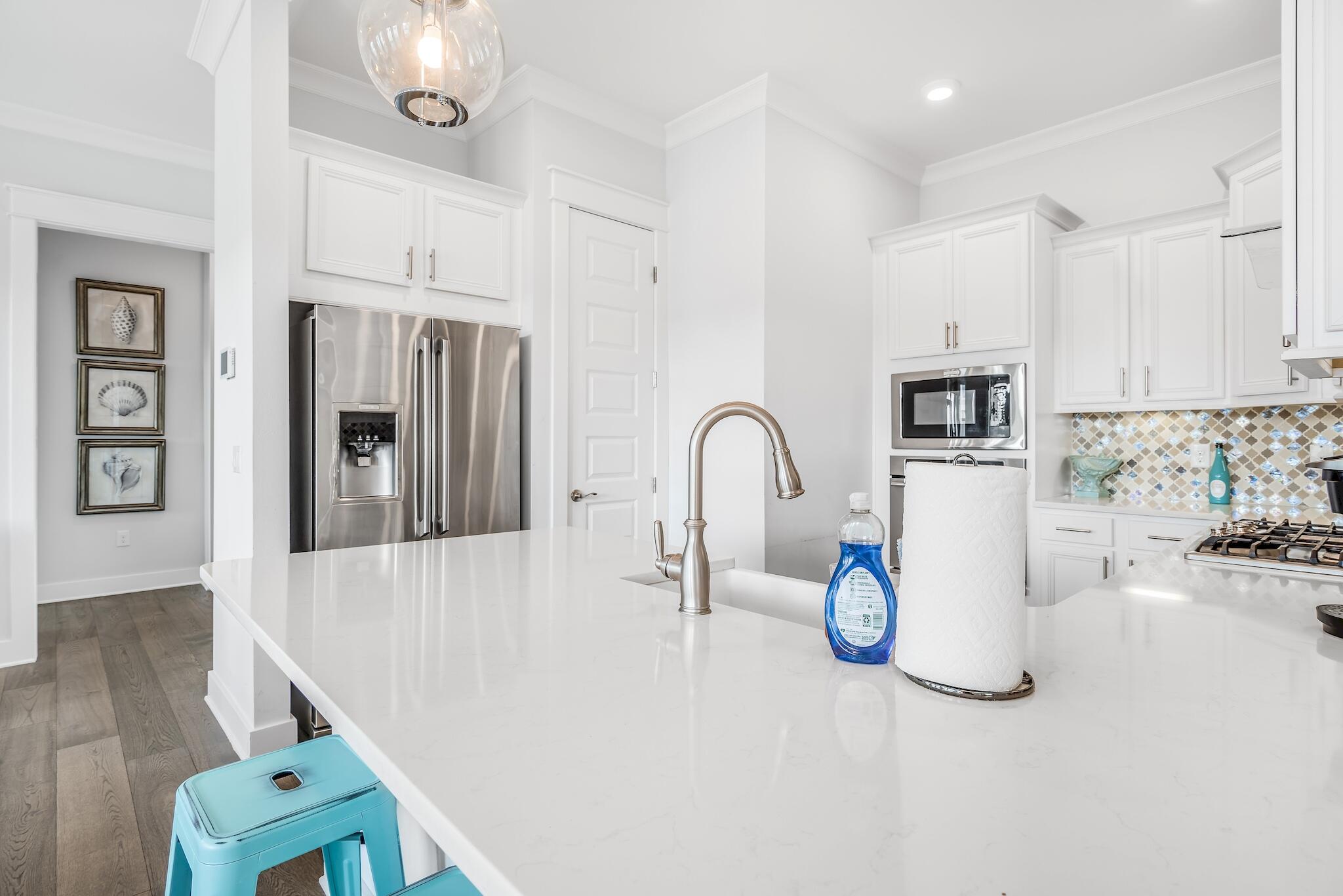 Bright white kitchen with a large quartz island, stainless appliances, and patterned tile backsplash.
