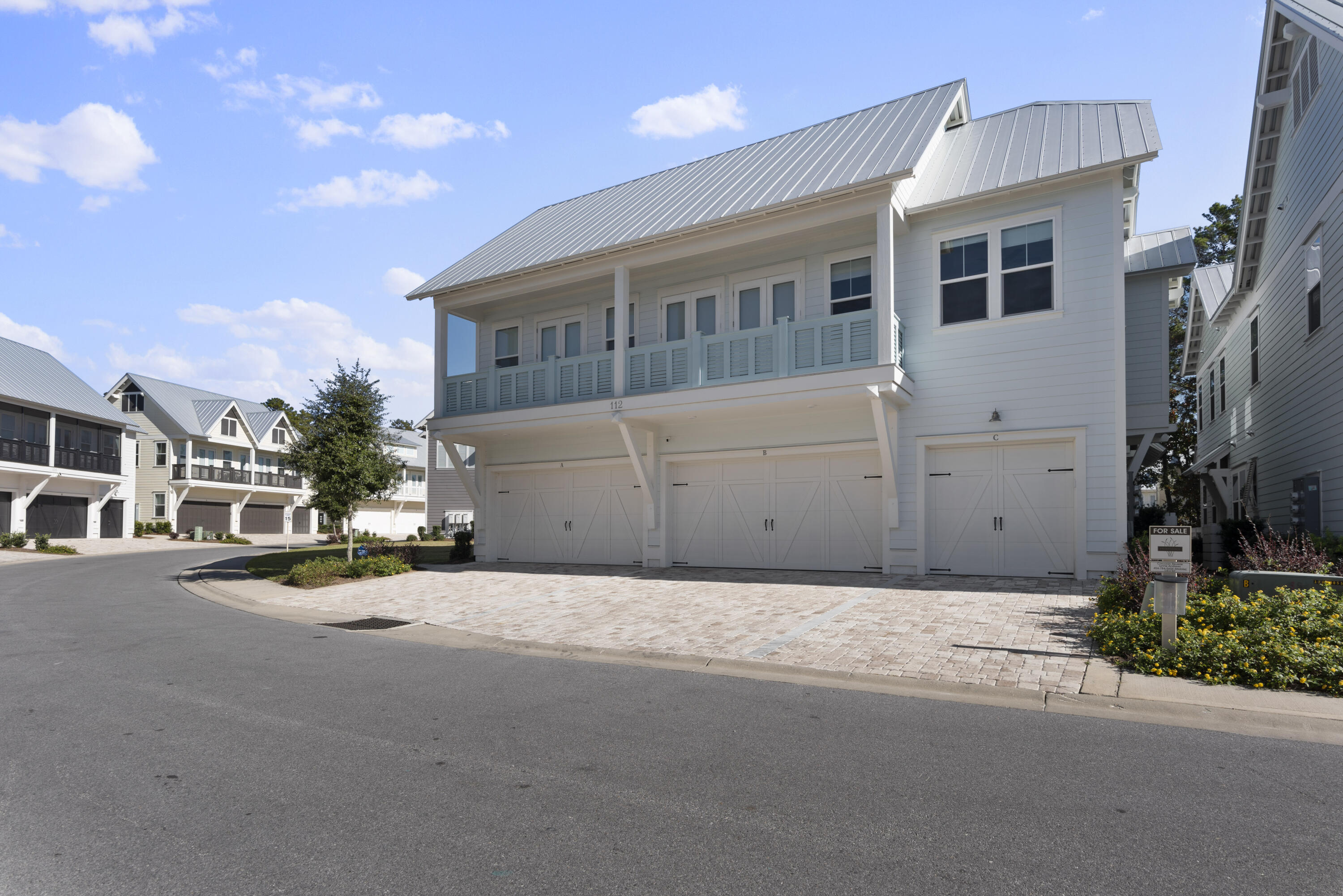 White multi-unit building with a metal roof, balcony, and garages labeled A, B, and C.