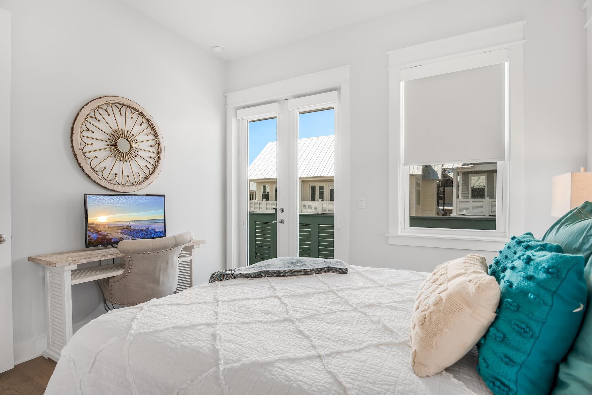 Bedroom with a white quilted bed, teal pillows, and glass doors overlooking a balcony.