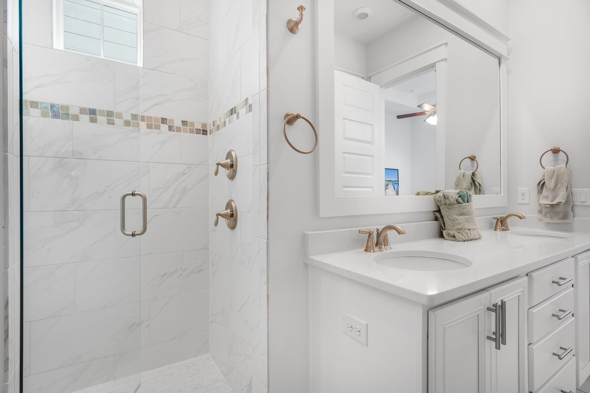 Bathroom with a marble-look tiled shower, mosaic accent band, and white vanity with gold-toned fixtures.