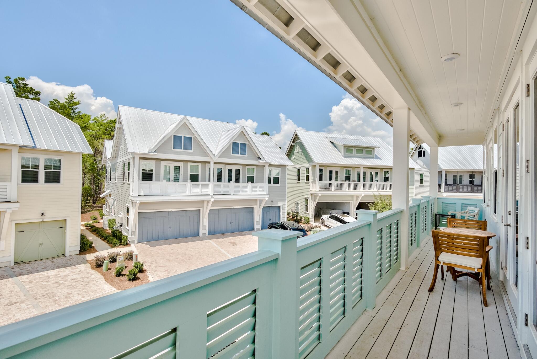 Covered balcony with aqua railings and wooden patio furniture overlooking neighboring homes.