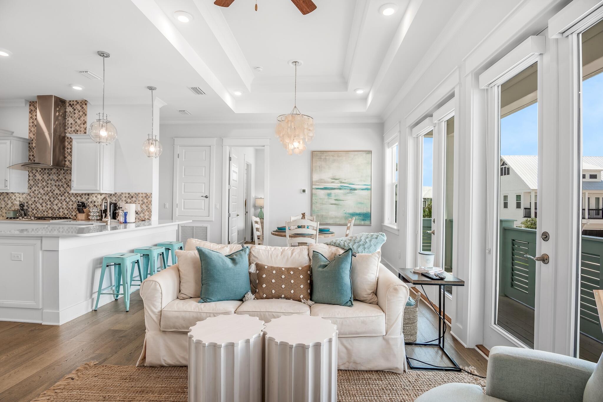 Open-plan living room and kitchen with a white sofa, turquoise stools, and large balcony doors.