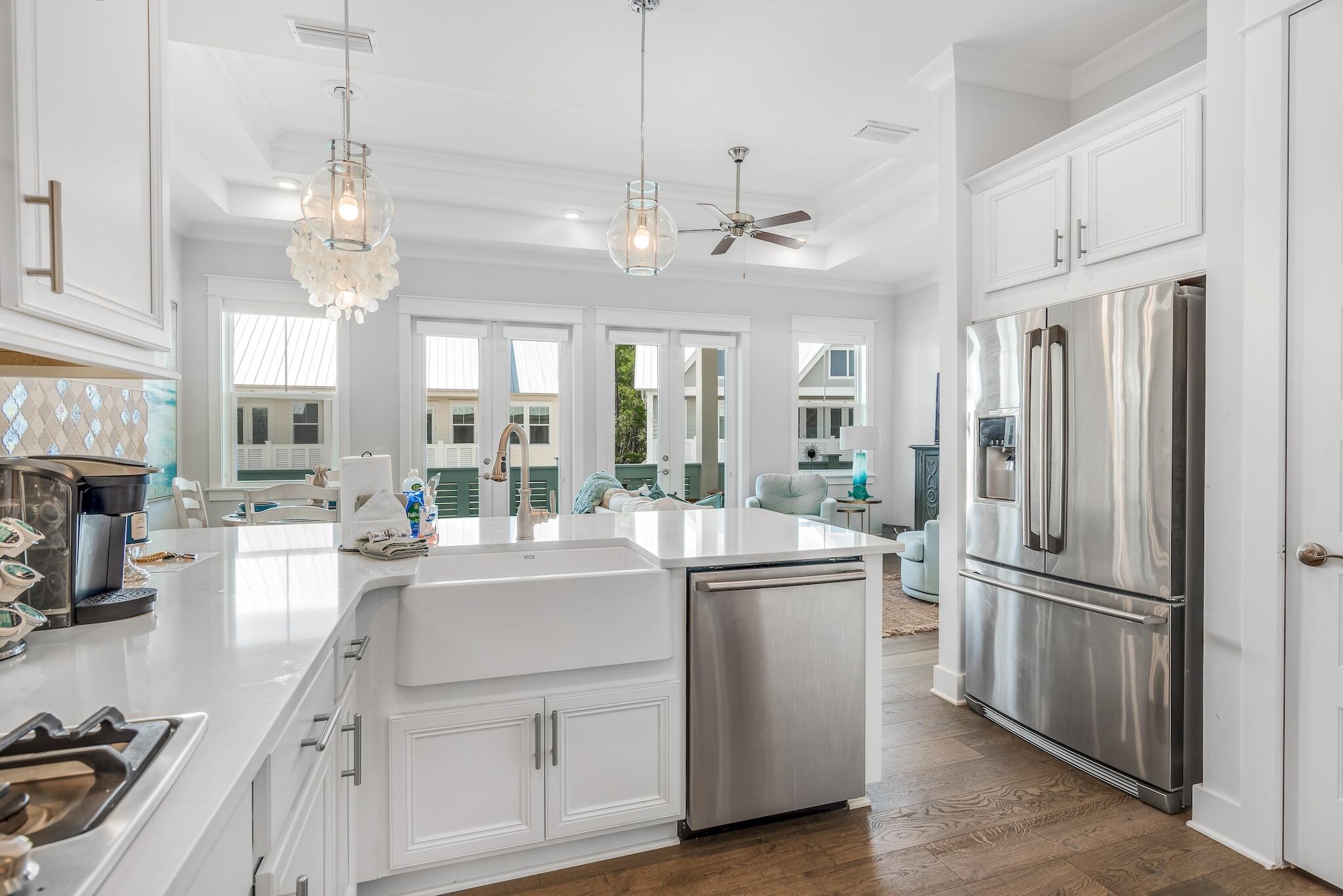 Bright white kitchen with a large island, farmhouse sink, stainless steel appliances, and windows opening to a sitting area.