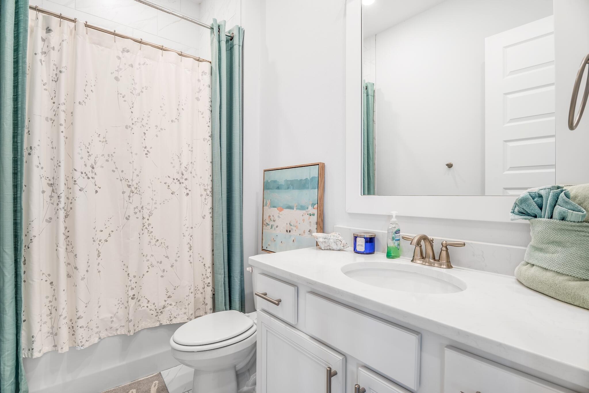 Bathroom with white vanity, bronze faucet, and bathtub behind a botanical shower curtain.
