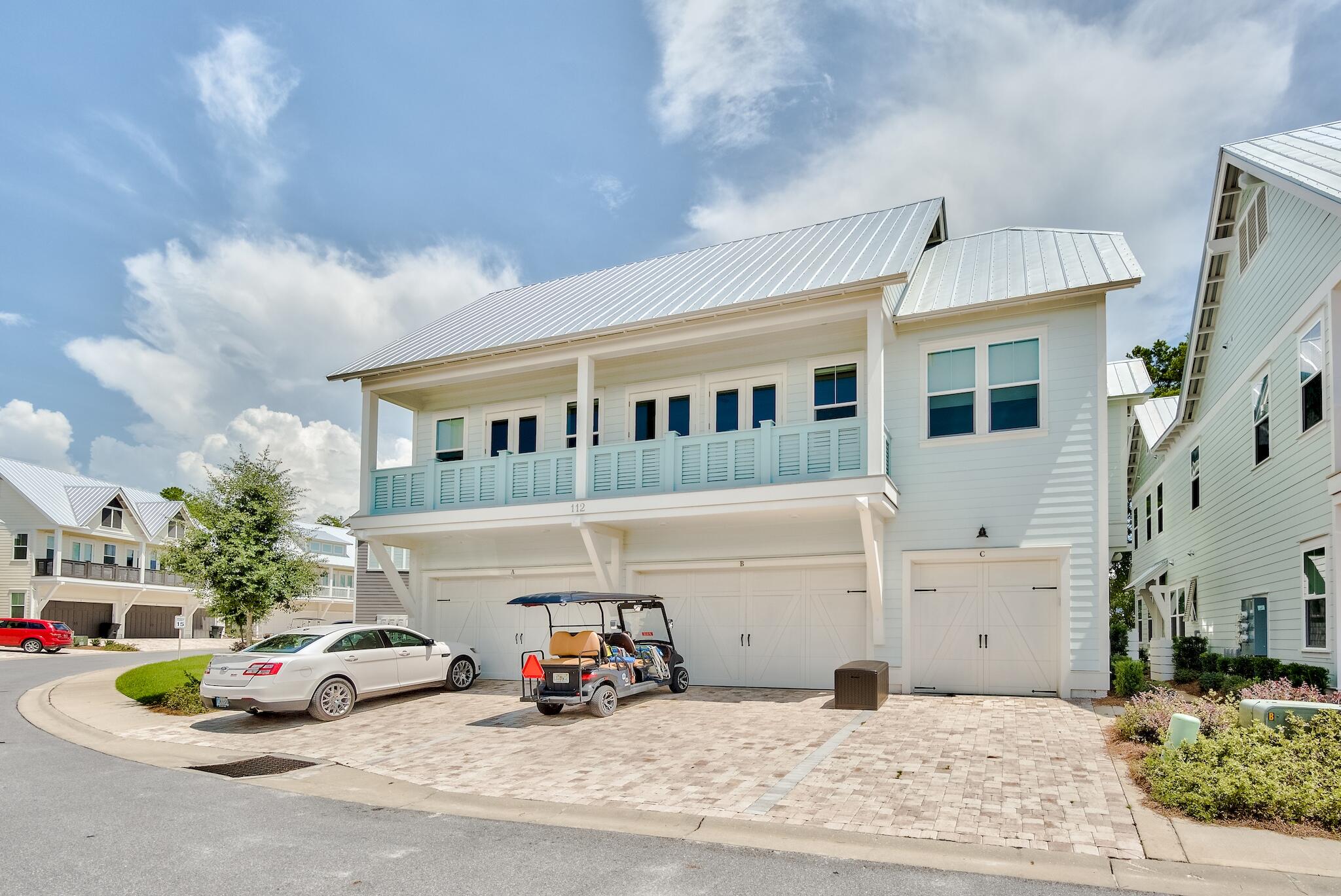 Light-colored coastal home with a metal roof, long balcony, three garages, and a golf cart in the driveway.