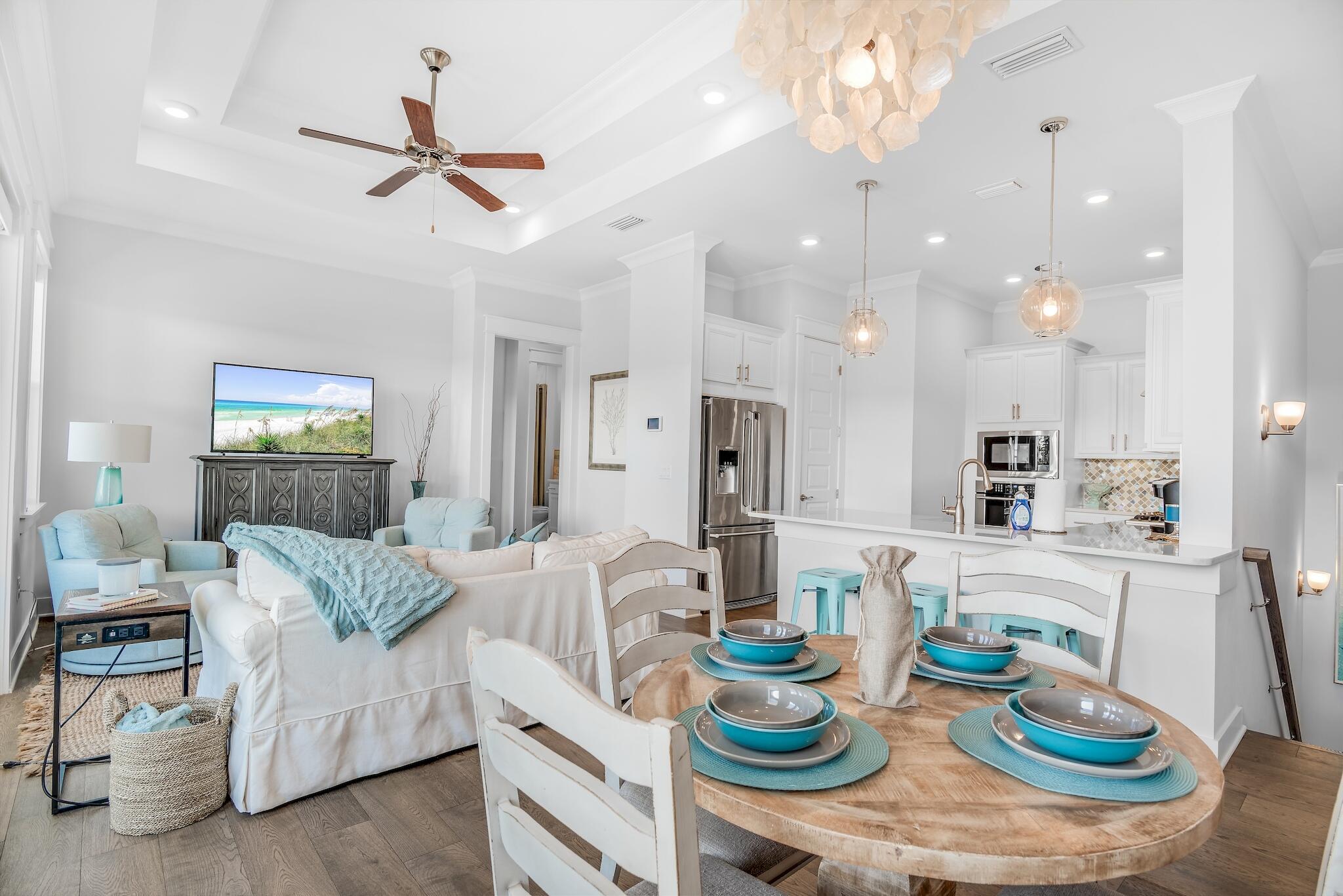Open-plan living and kitchen area with pale blue seating, a white island, and a round dining table set with turquoise dishes.
