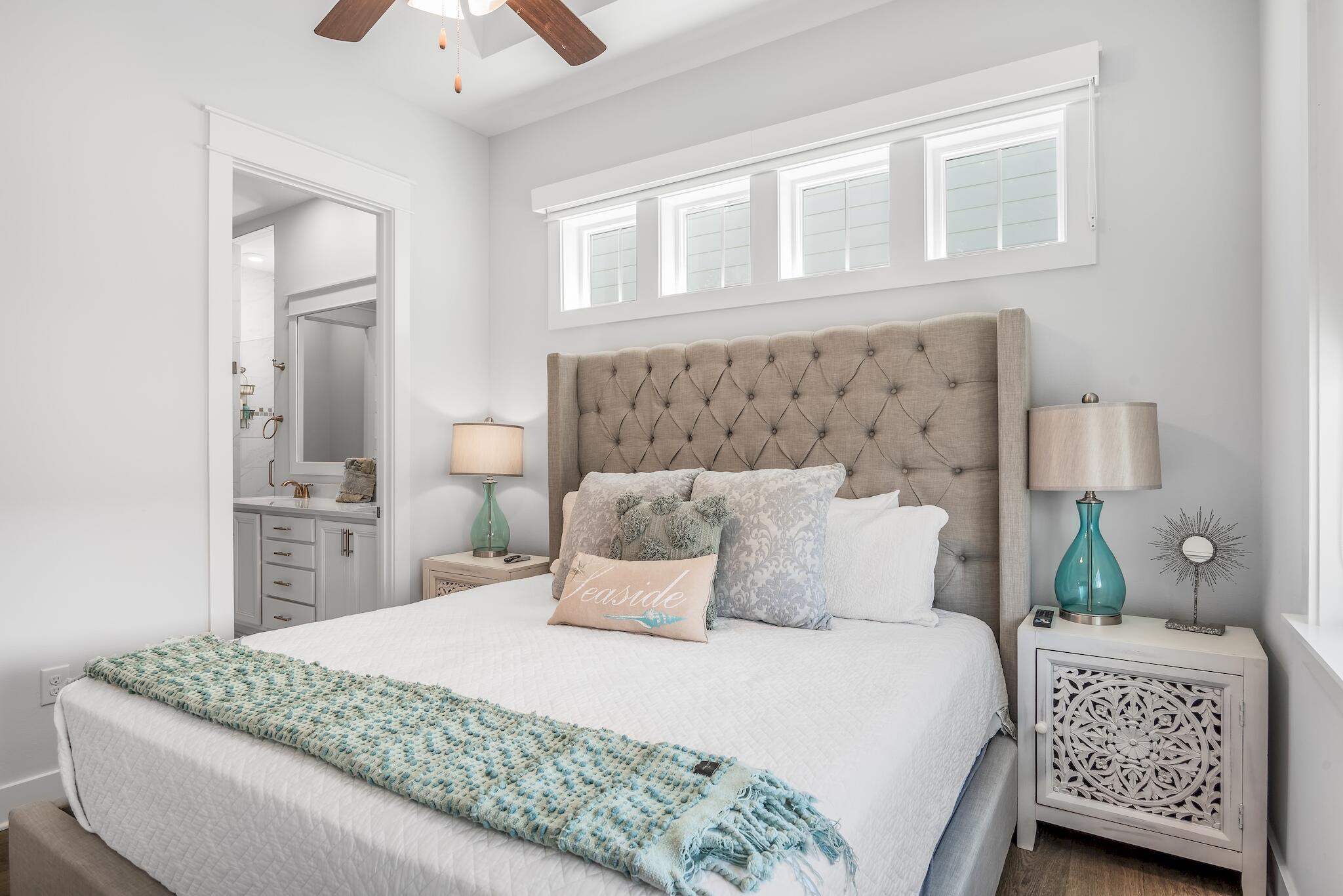 Bedroom with a tufted beige headboard, aqua throw, and doorway to an adjoining bathroom.