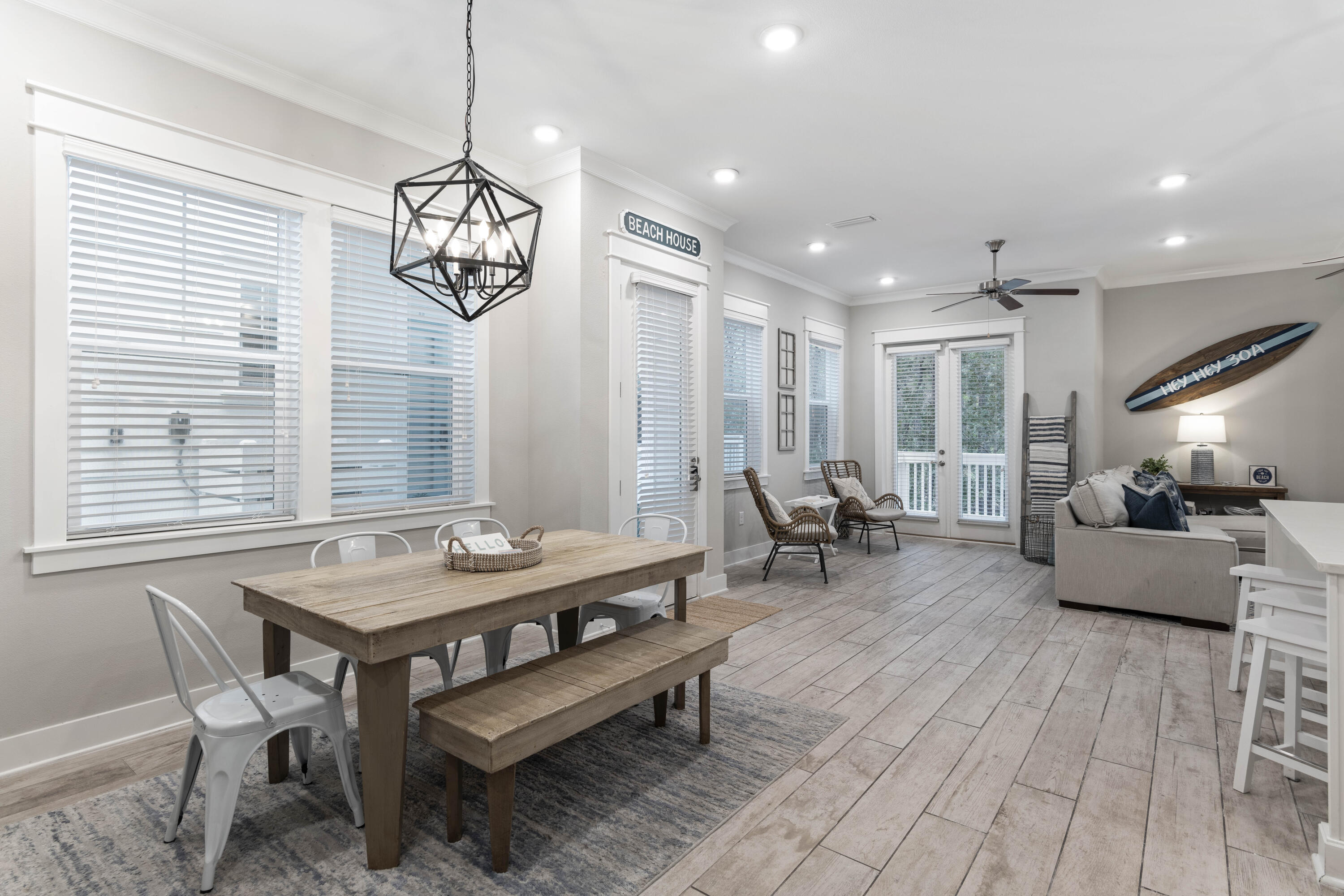 Open-plan dining and living area with a rustic table, wicker chairs, and coastal decor.