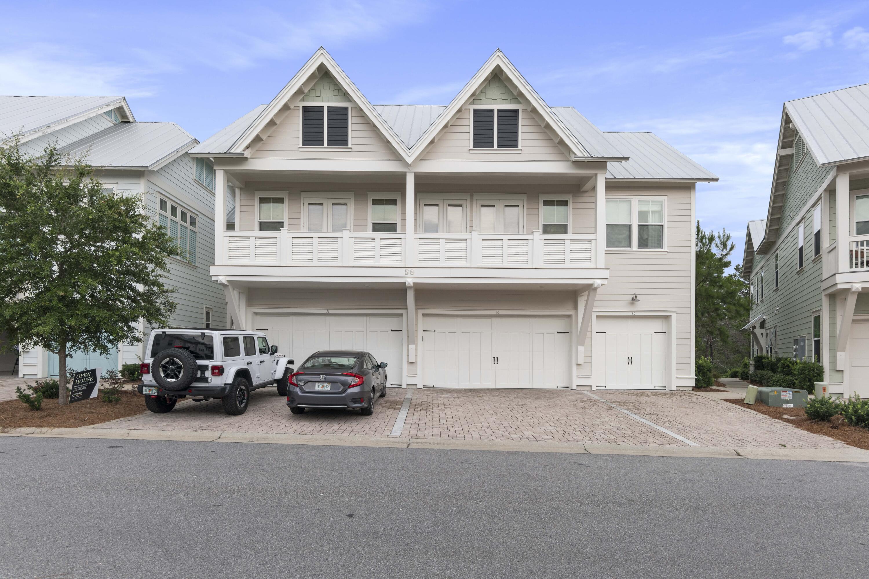 Coastal townhouse with twin gables, a covered balcony, three garage doors, and a brick-paver driveway.