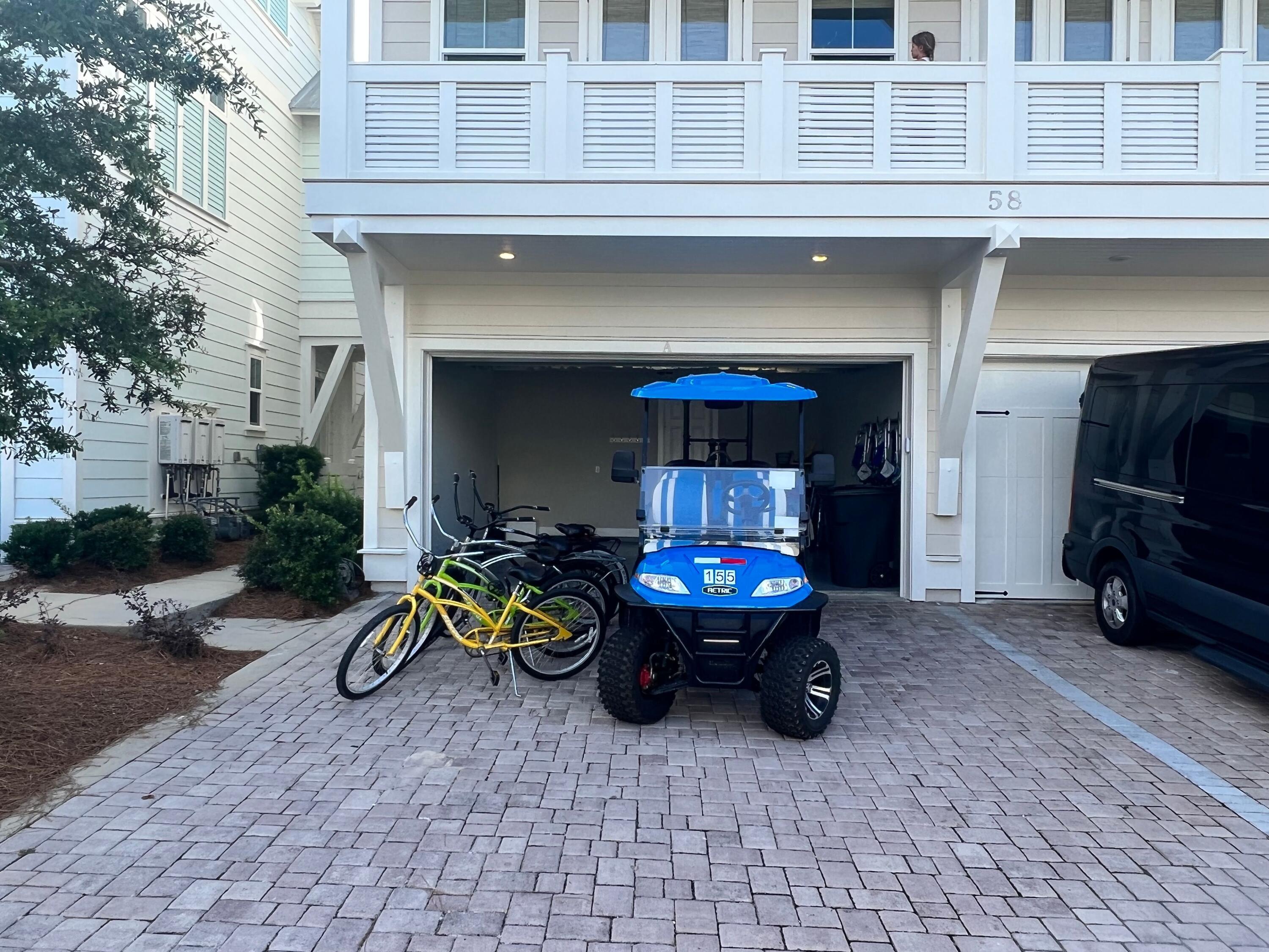 Raised balcony above an open garage, with a blue golf cart and bicycles on the paver driveway.