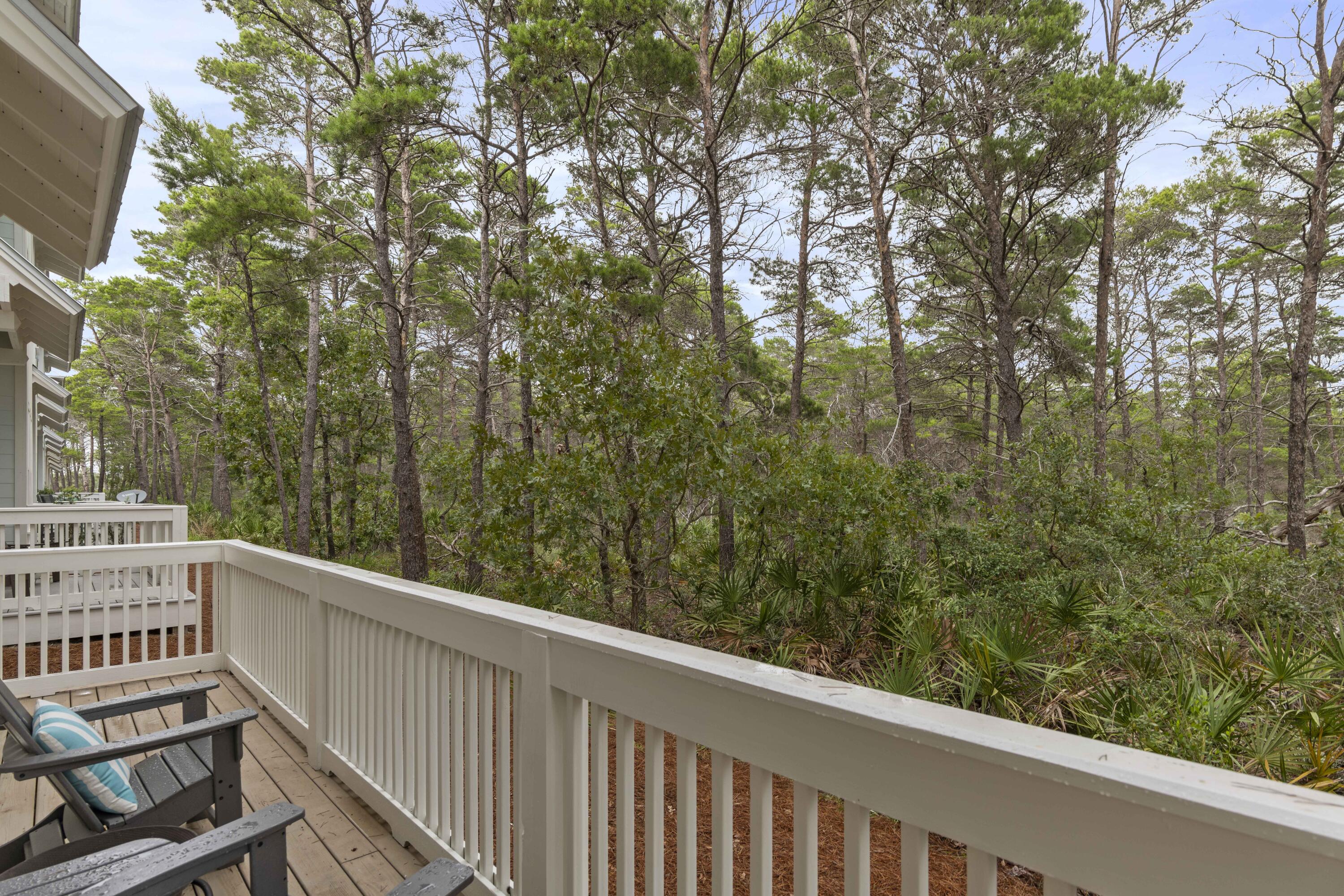 Wooden deck overlooking pine woodland, with white railings and Adirondack chairs.