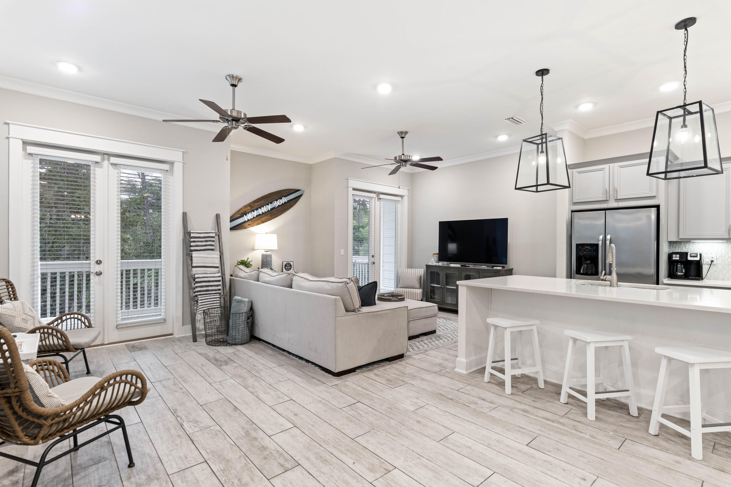 Open-plan living room and kitchen with a pale sectional, white island, and wall-mounted surfboard.