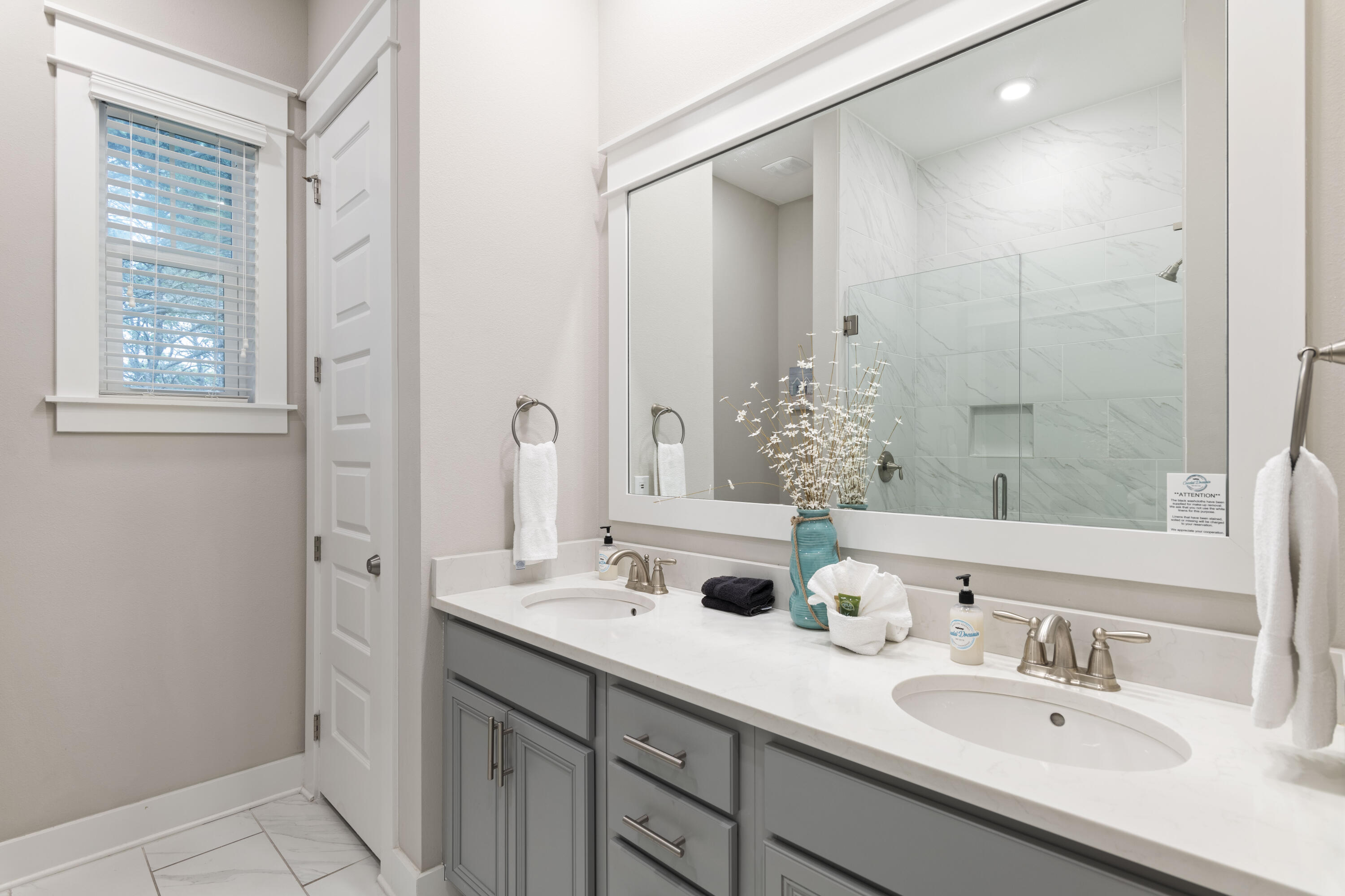 Bathroom with a gray double-sink vanity and glass shower lined with marble-look tile.