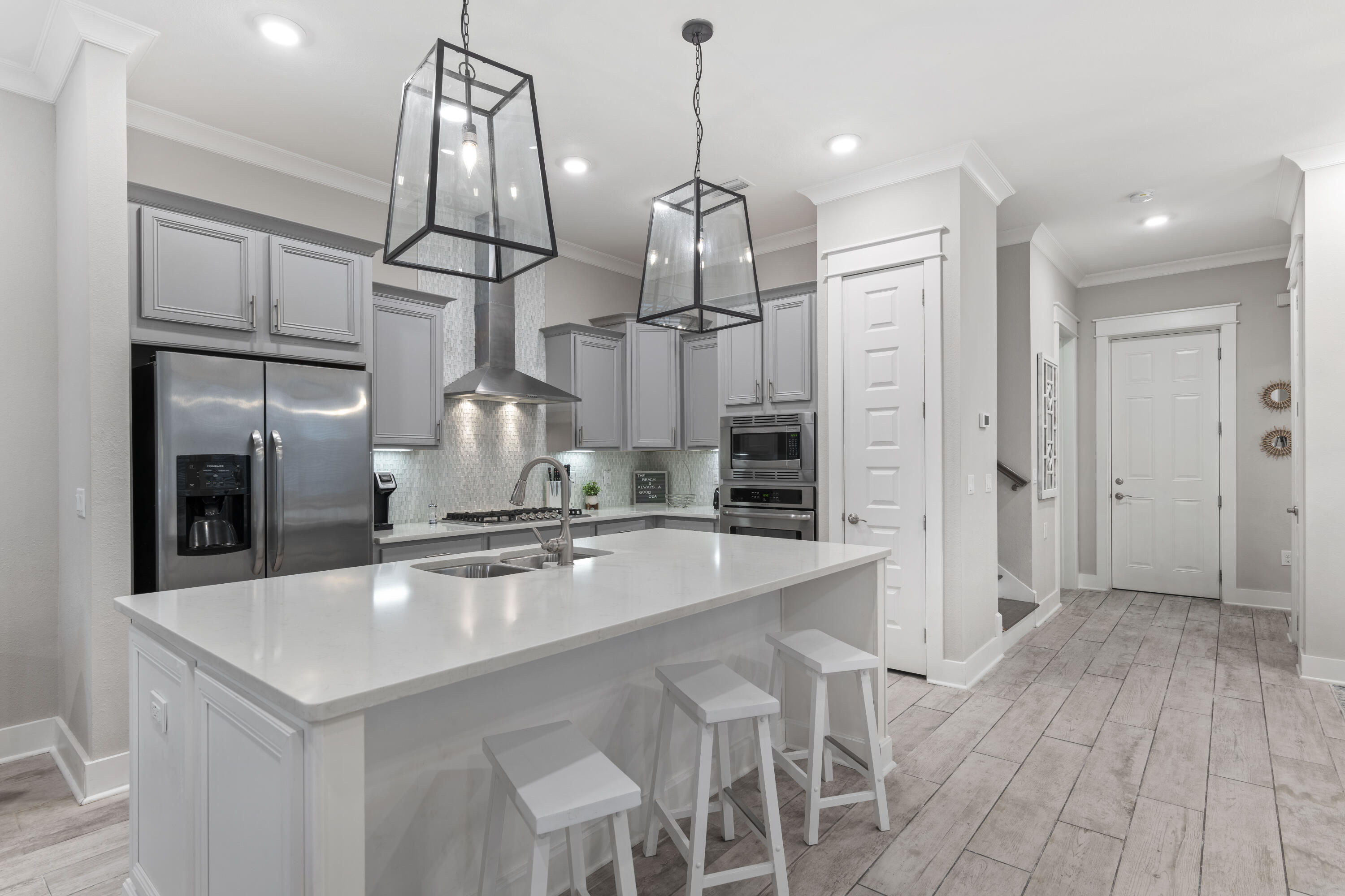Modern kitchen with a large white island, gray cabinets, stainless appliances, and glass pendant lights.