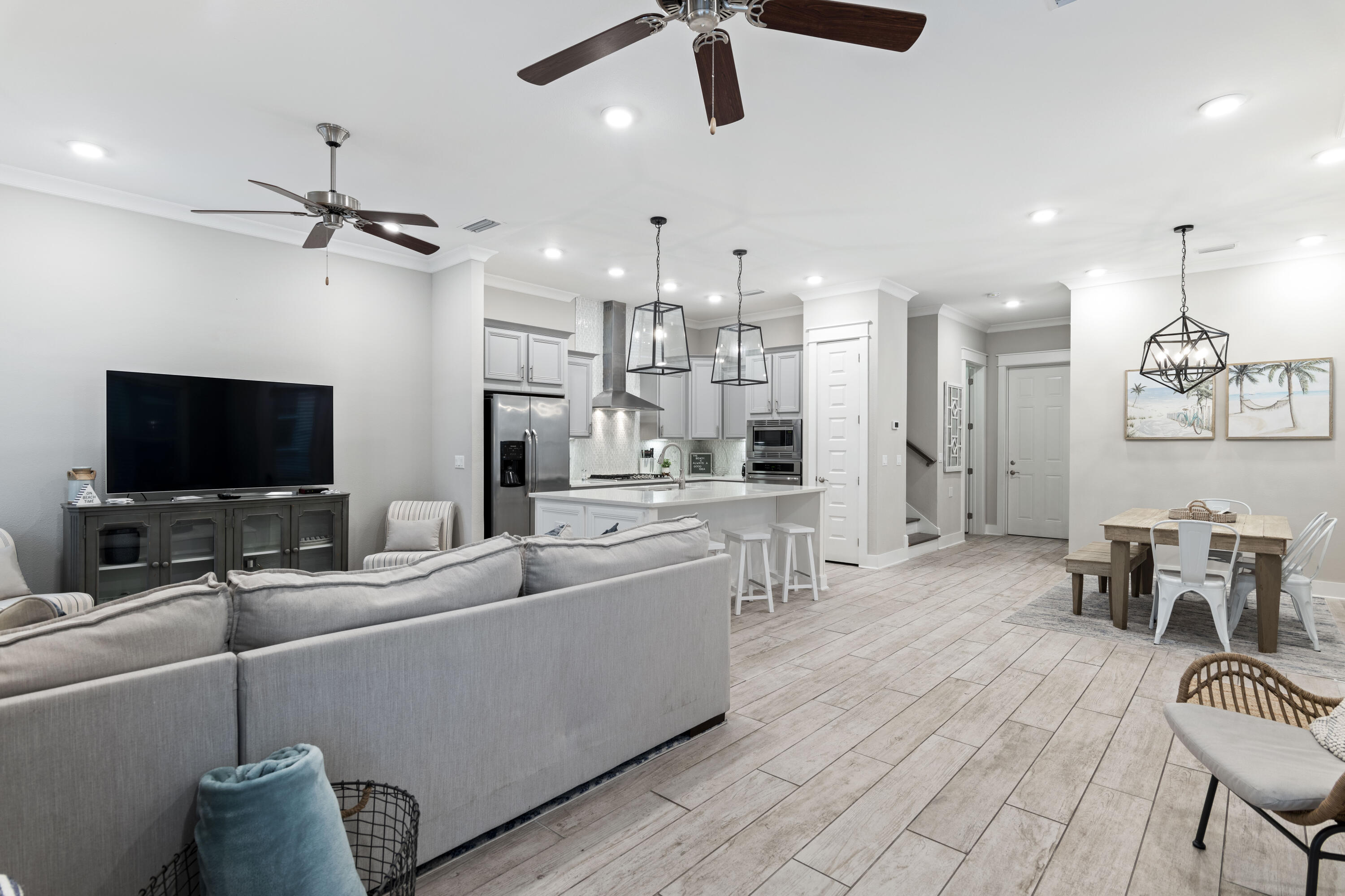 Open-plan living room and kitchen with a gray sectional, white island, and wood-look tile floors.