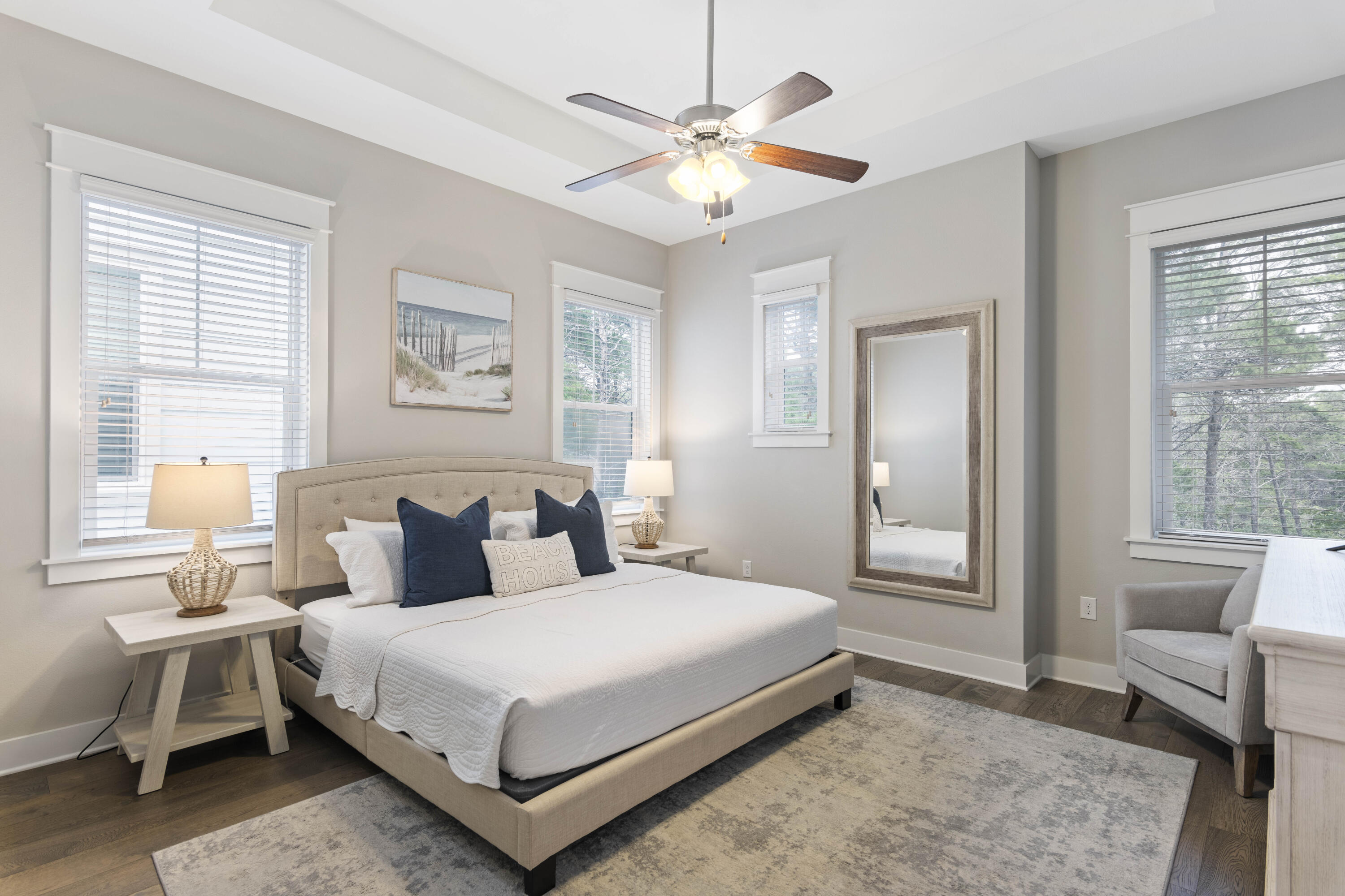 Bedroom with a king bed, navy pillows, beach artwork, and multiple bright windows.