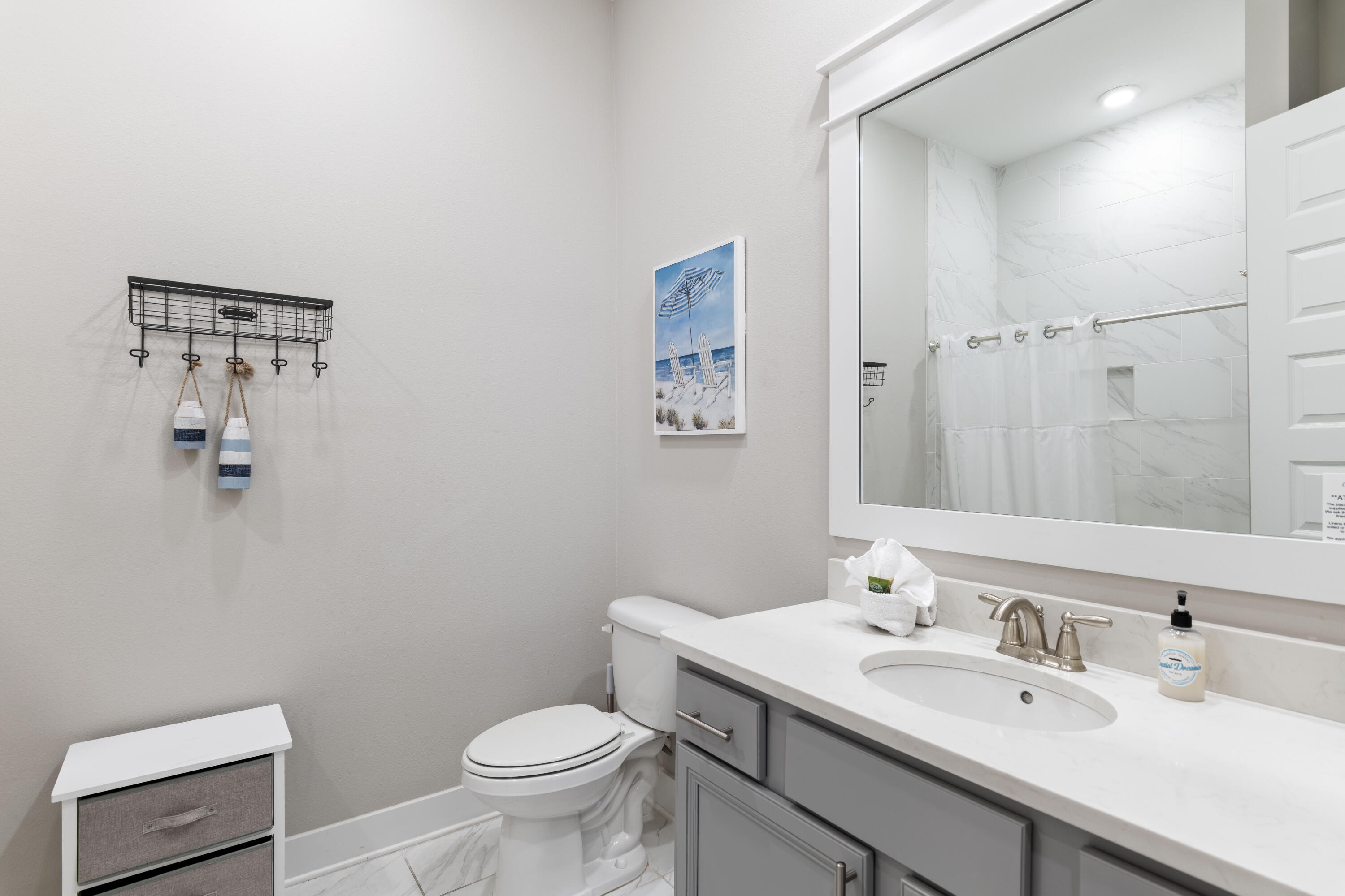 Bathroom with gray vanity, white countertop, and marble-look tiled shower.
