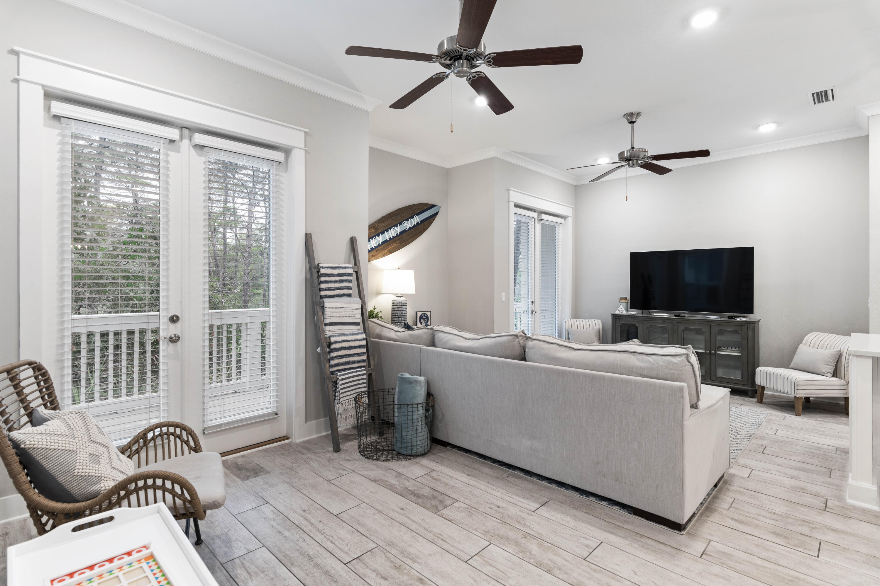 Furnished living room with a gray sofa, wicker chairs, shuttered windows, and decorative surfboard.