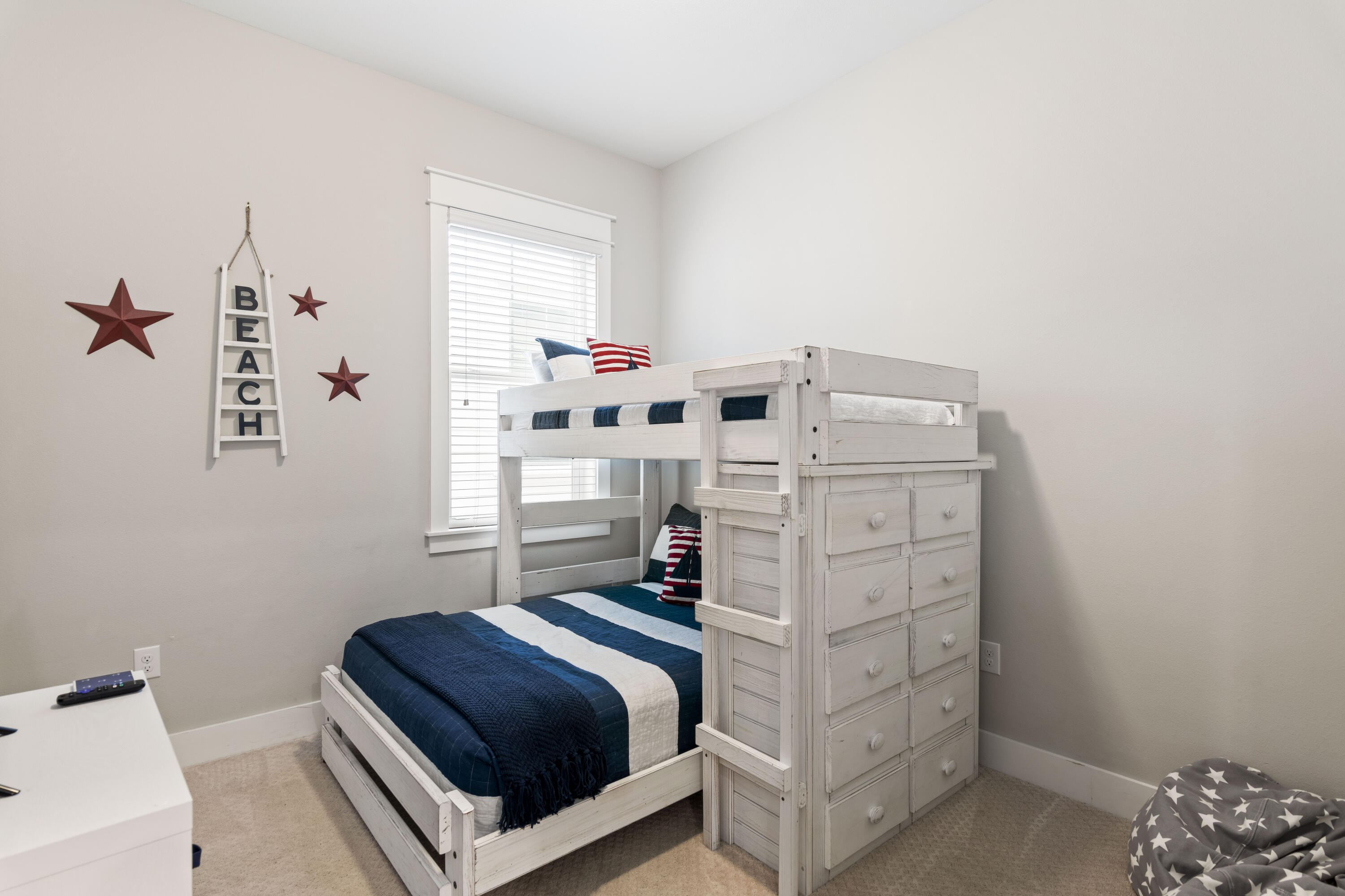 Bedroom with a white bunk bed, built-in drawers, striped navy bedding, and beach-themed wall decor.