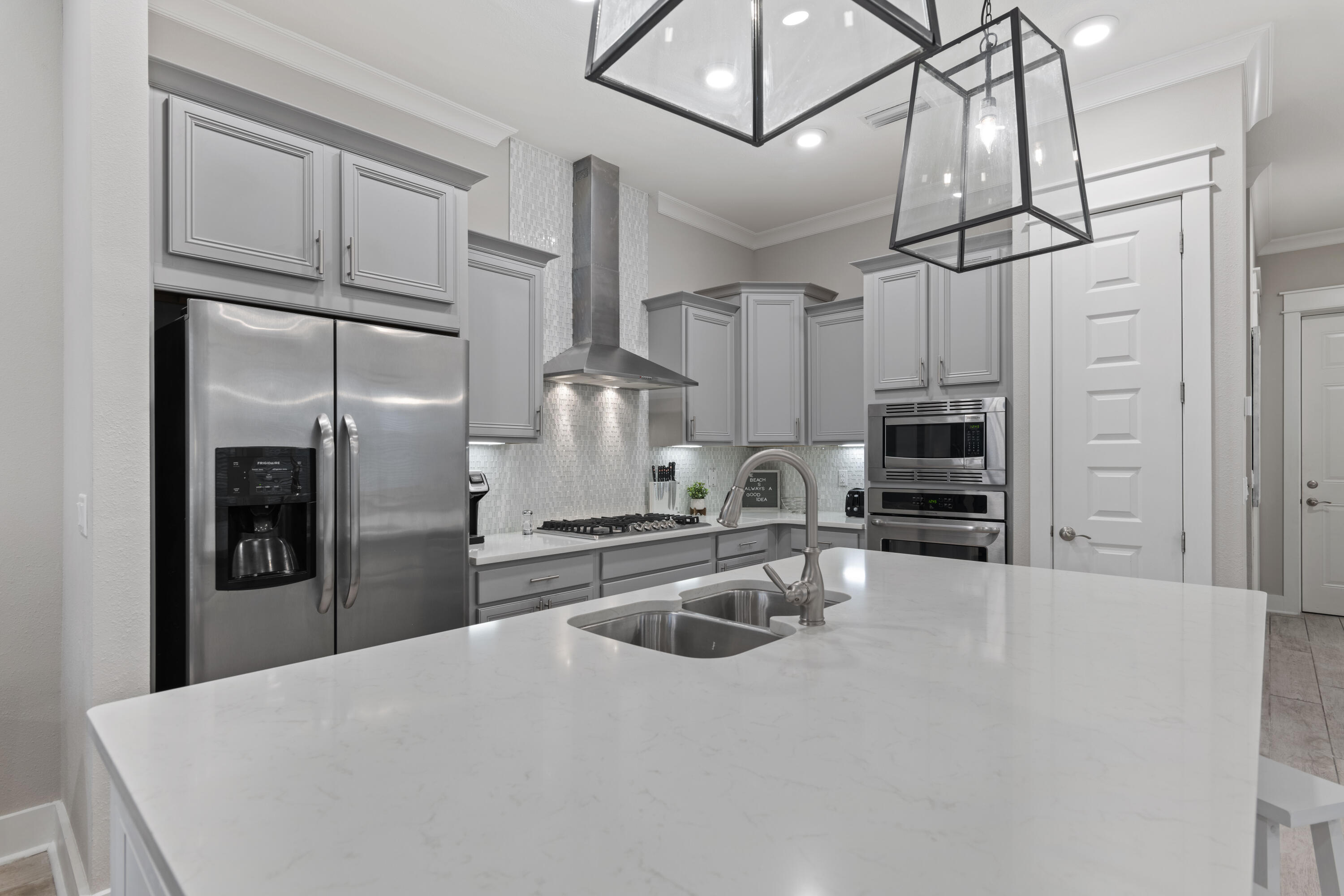 Kitchen with gray cabinets, stainless appliances, and a large white island with a double-basin sink.