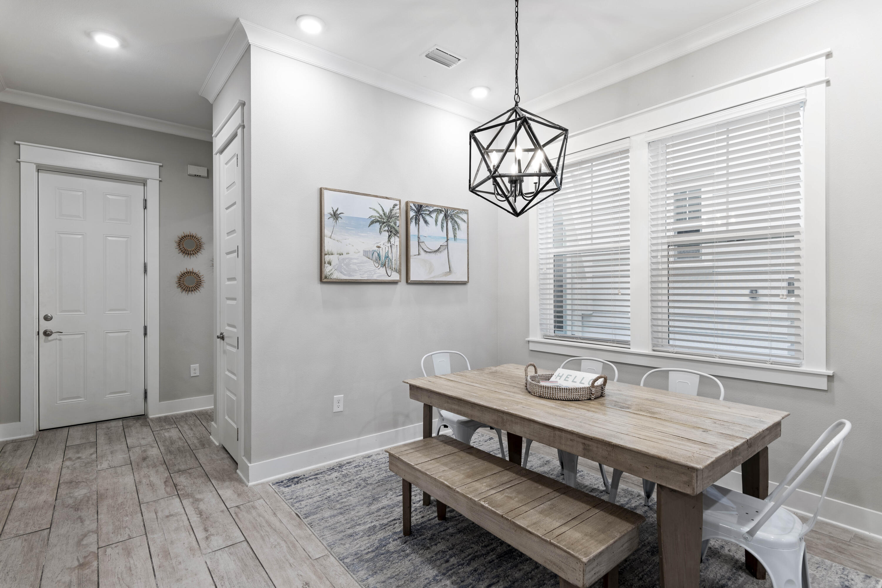 Dining room with a rustic wood table, bench, white chairs, and geometric pendant light.