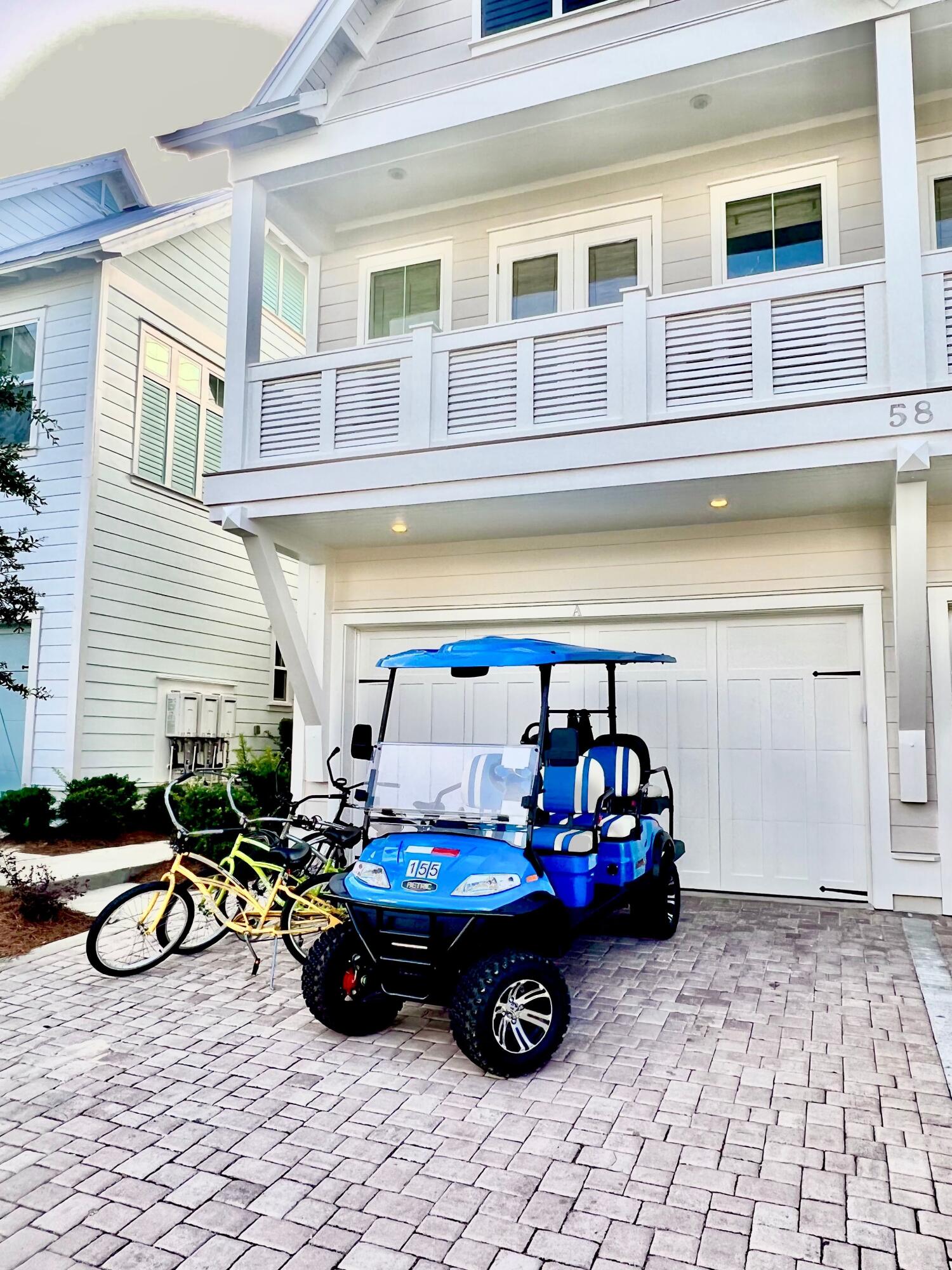 Townhouse exterior with a balcony, garage, blue golf cart, and bicycles in the paved driveway.