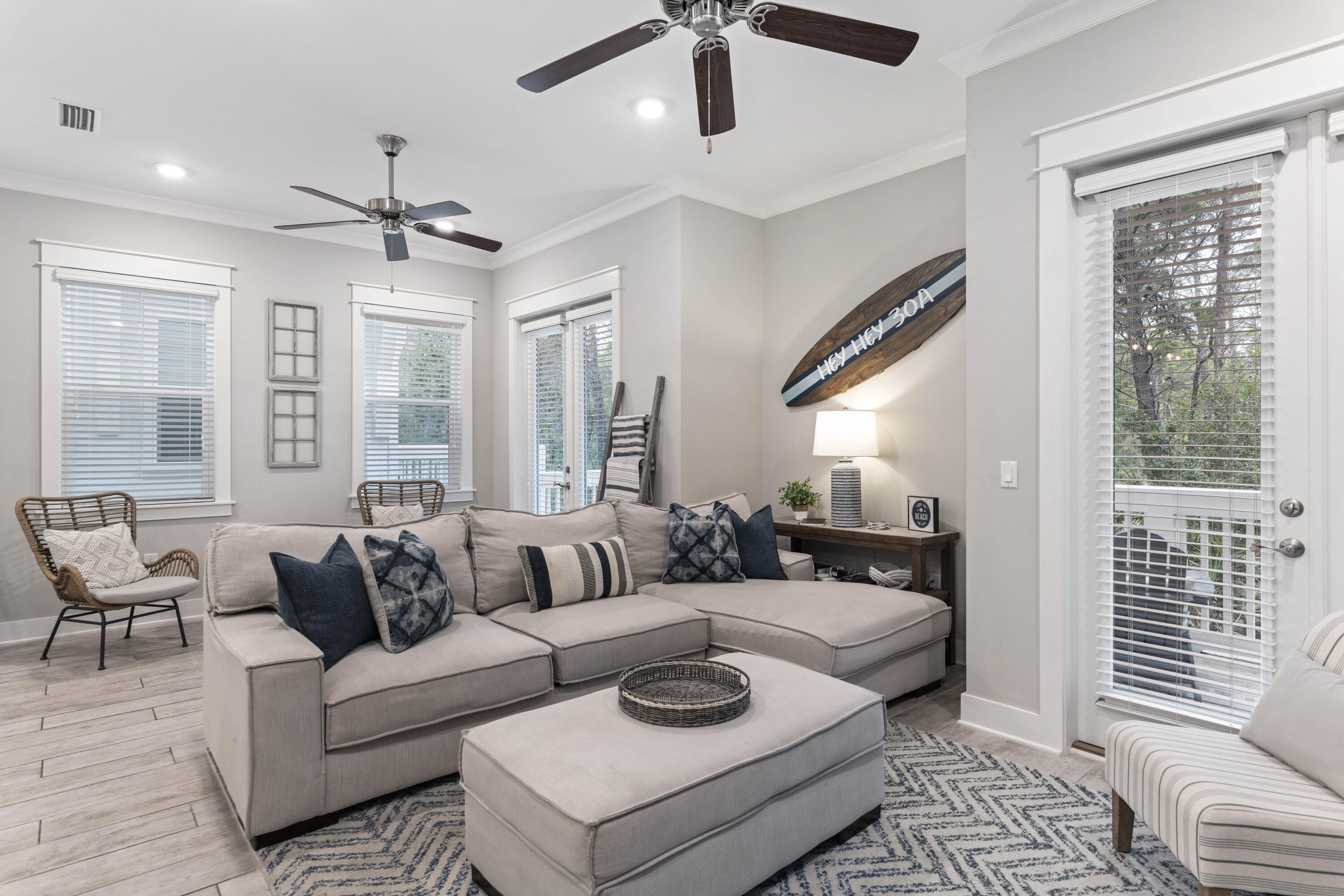 Staged living room with a gray sectional, blue patterned rug, and decorative Hwy 30A surfboard.