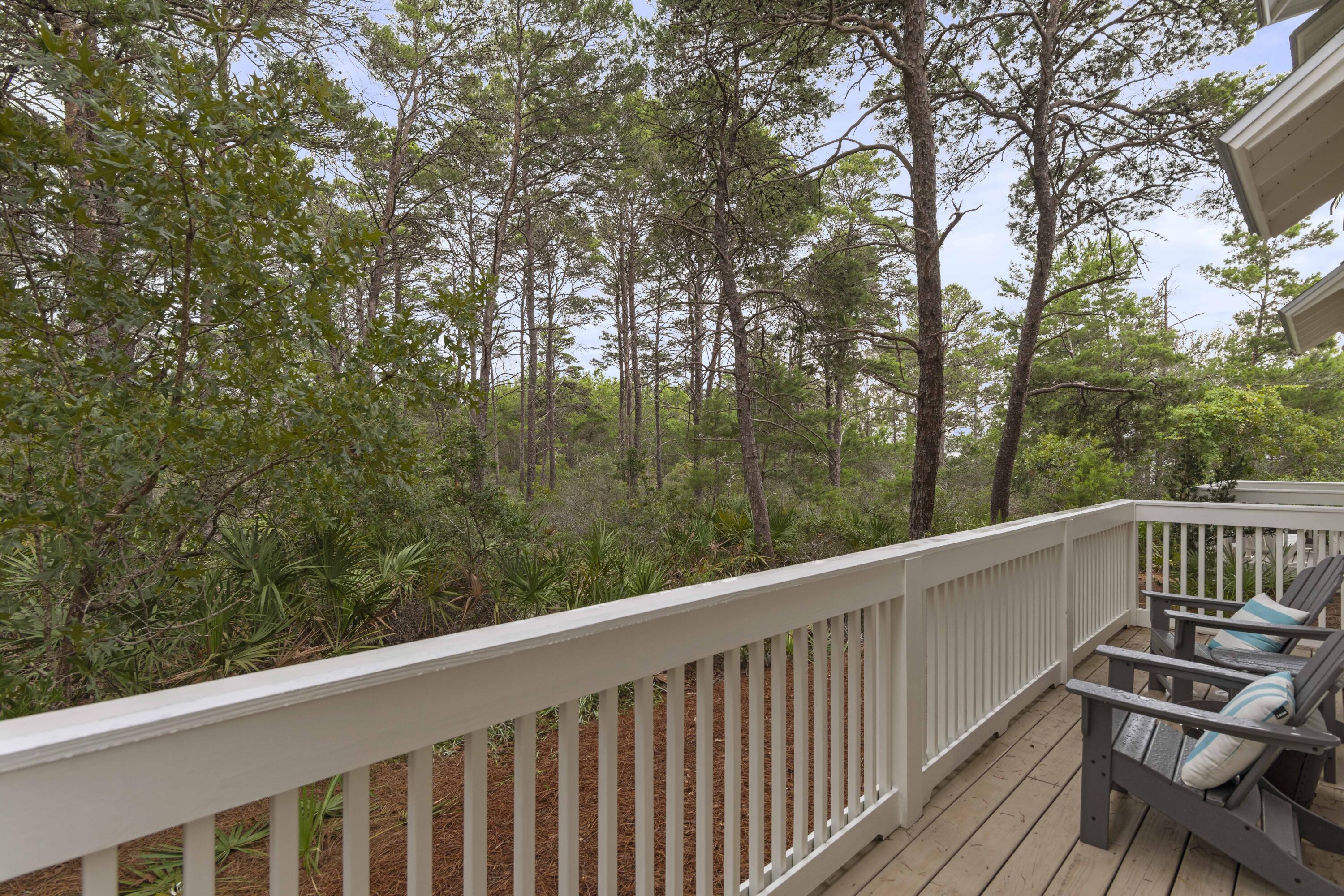 Outdoor deck with white railings and Adirondack chairs overlooking a wooded area.