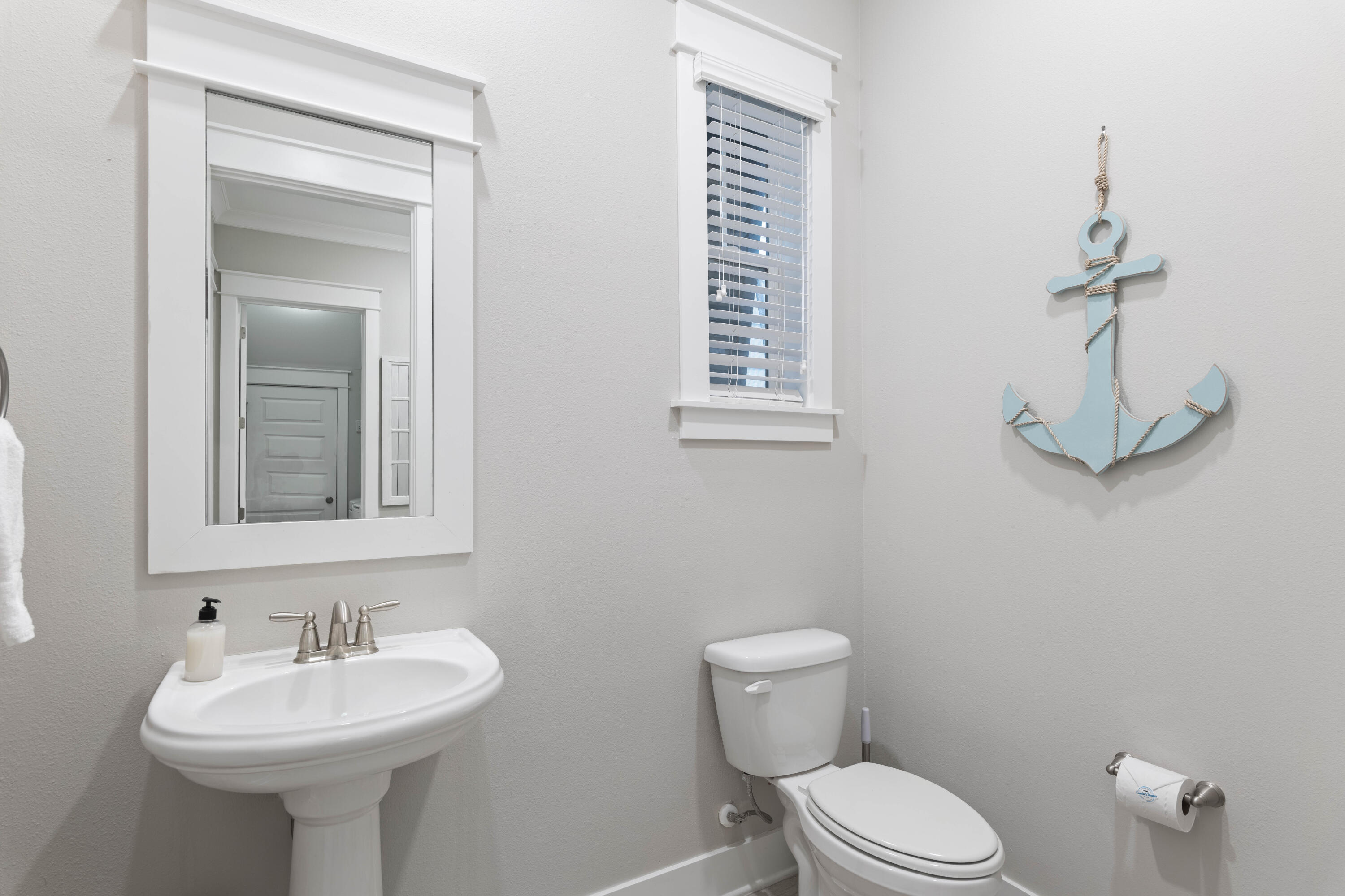 Bathroom with a pedestal sink, toilet, window blinds, and blue anchor wall decoration.