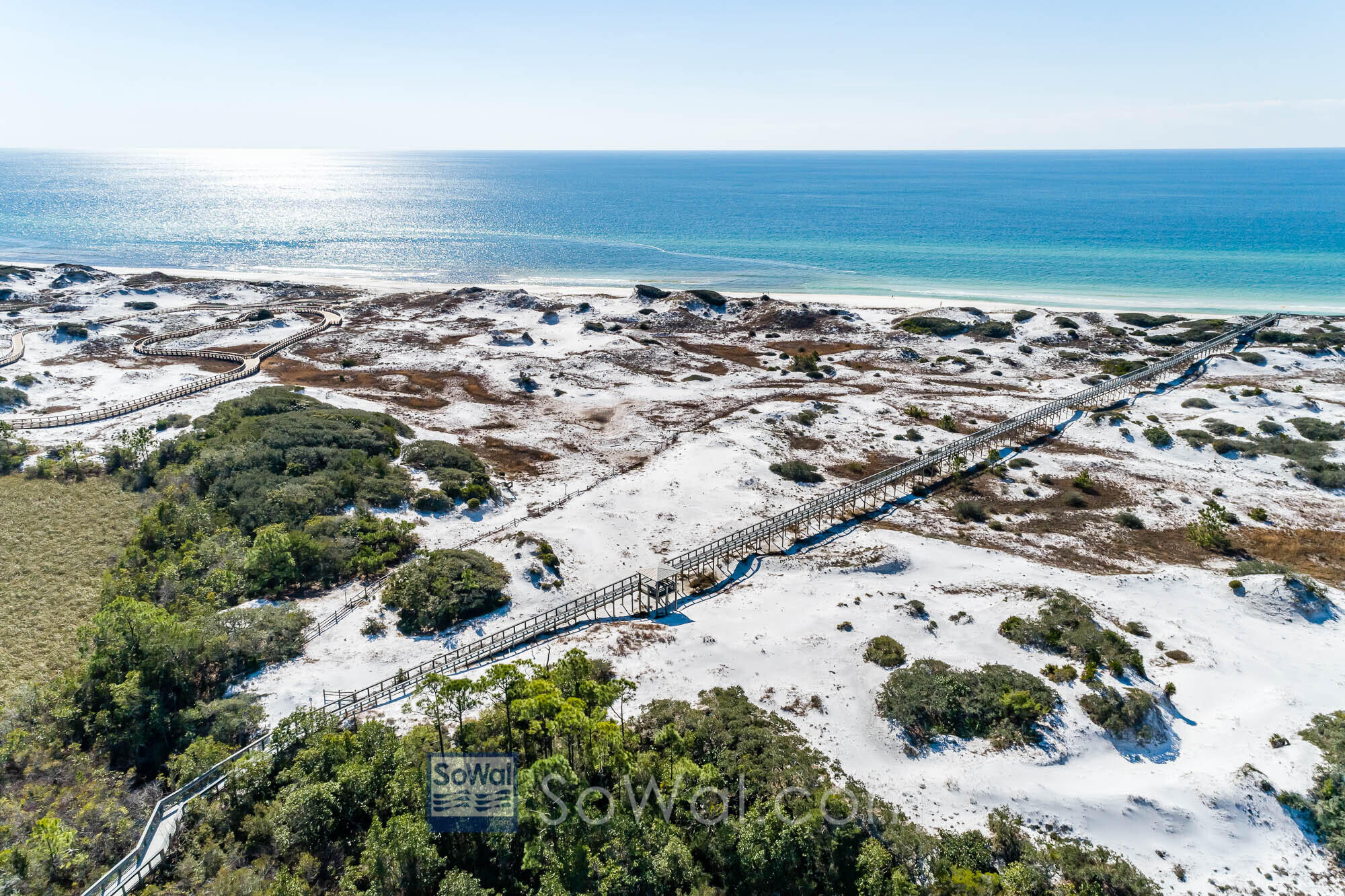 Aerial view of boardwalks crossing sandy dunes toward the blue Gulf shoreline.