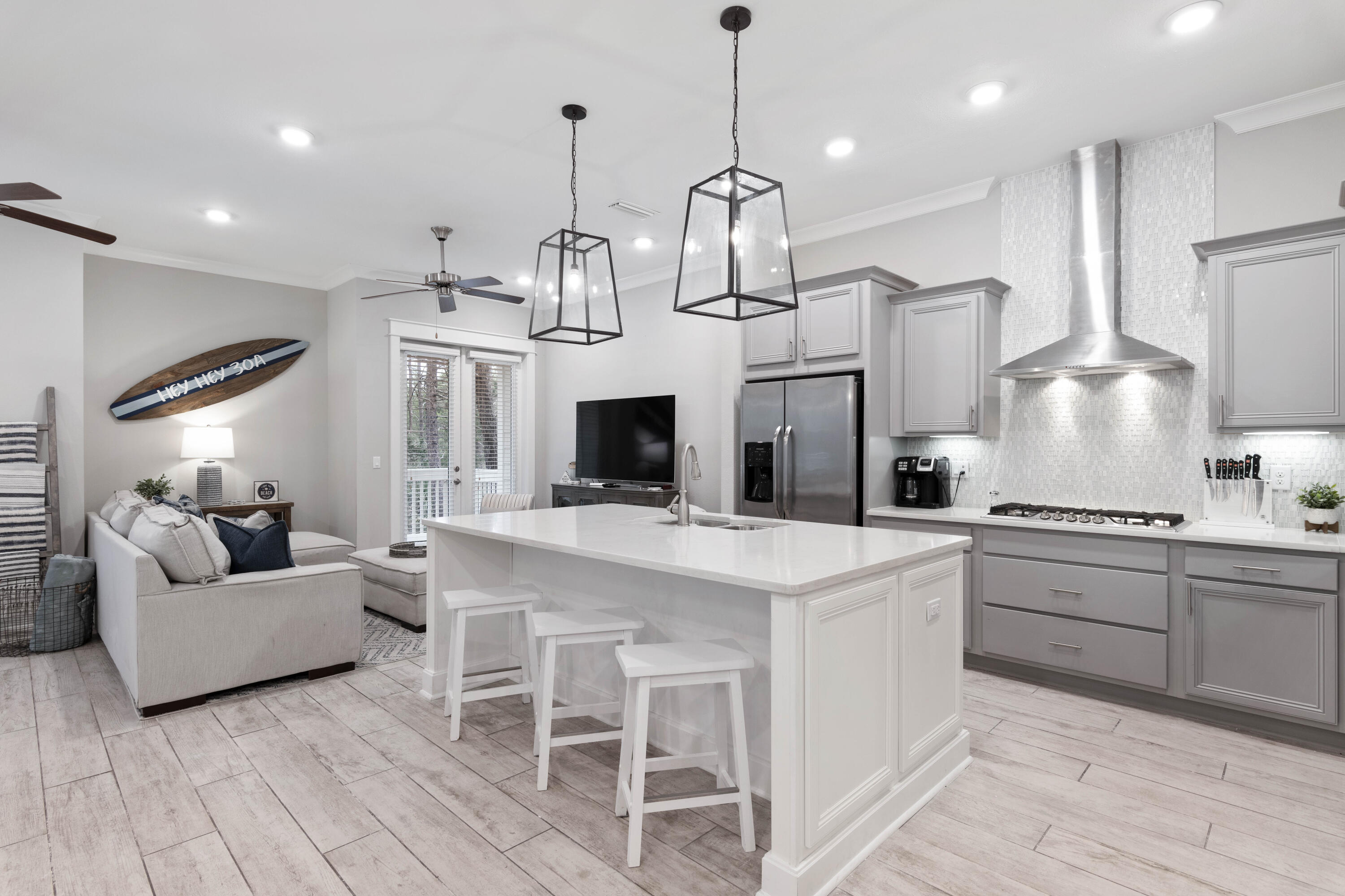 Open kitchen and living area with a large white island, gray cabinets, stainless appliances, and sofa seating.