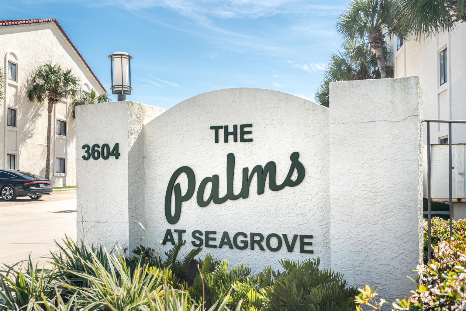 The Palms at Seagrove entrance sign beside condominium buildings and palm landscaping.