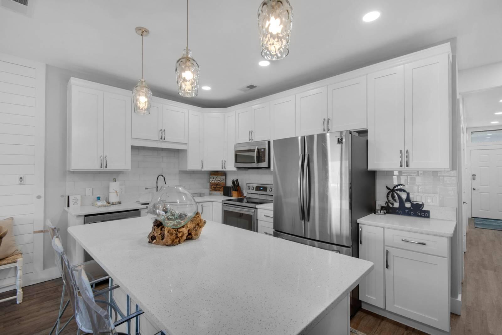 Kitchen with white cabinets, stainless steel appliances, and a large quartz island topped with a glass centerpiece.