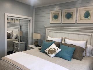 Staged bedroom with a paneled gray headboard wall, teal accent pillows, and framed botanical prints.