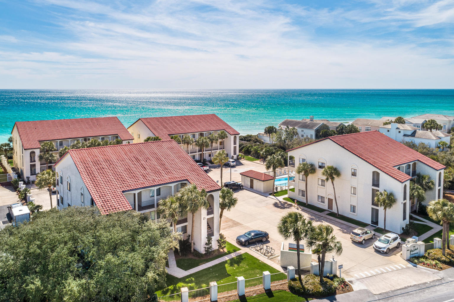 Beachfront condominium complex with red tile roofs, palm-lined grounds, and turquoise Gulf water.
