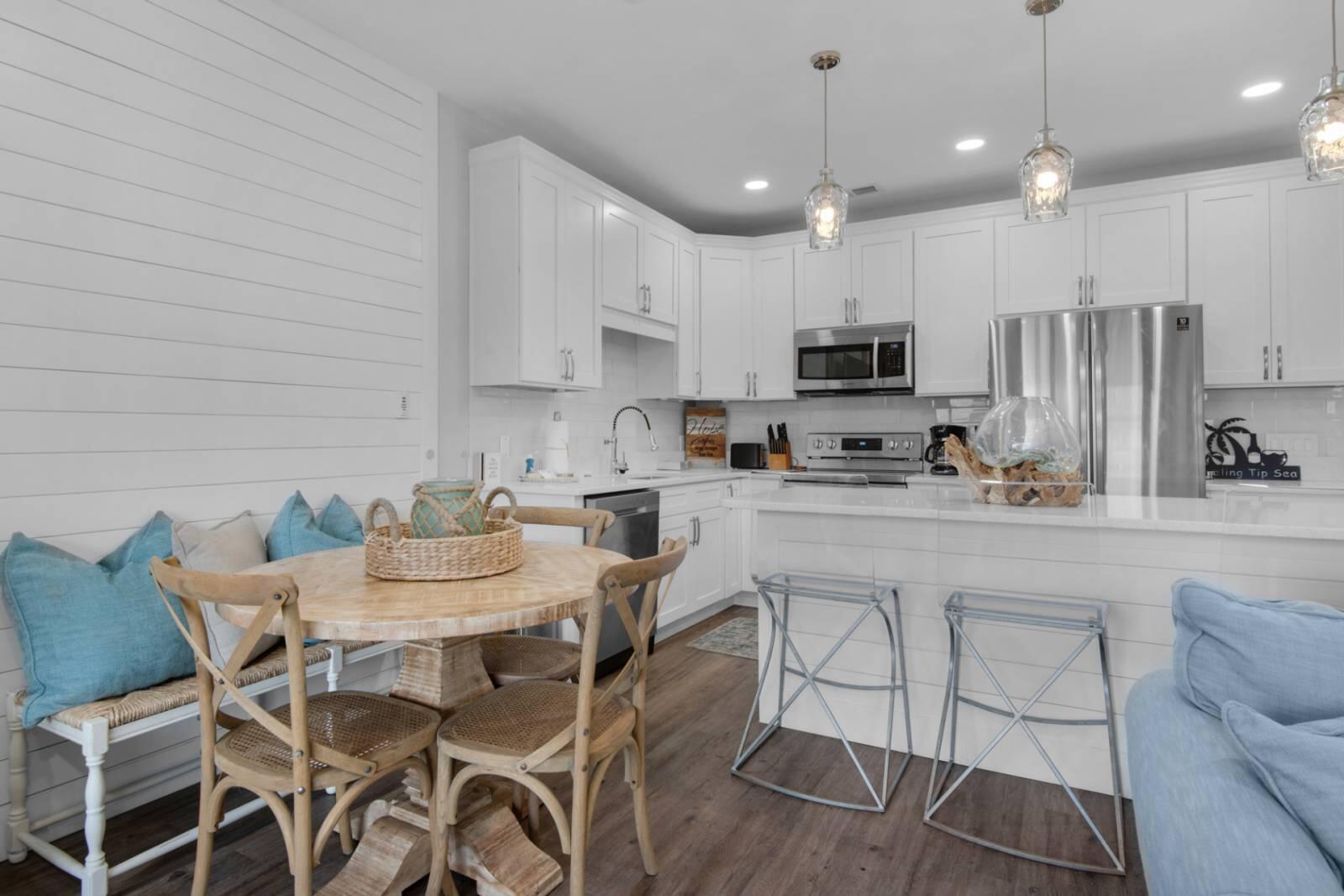 Kitchen with white cabinetry, stainless steel appliances, breakfast bar, and a round dining table beside a blue-cushioned bench.