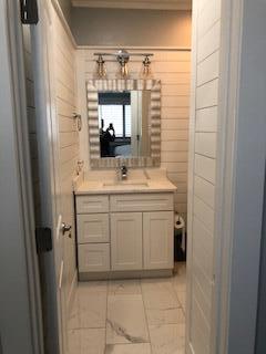 Bathroom with a white vanity, framed mirror, wall sconces, and pale marble-look tile floor.
