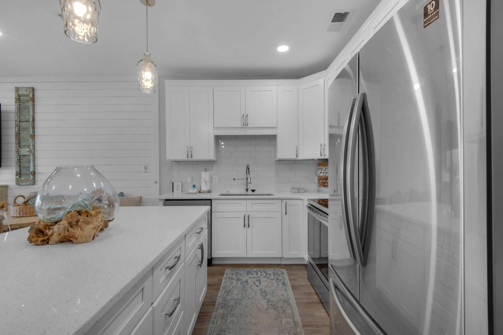 Modern white kitchen with a large island, stainless steel appliances, and pendant lights.